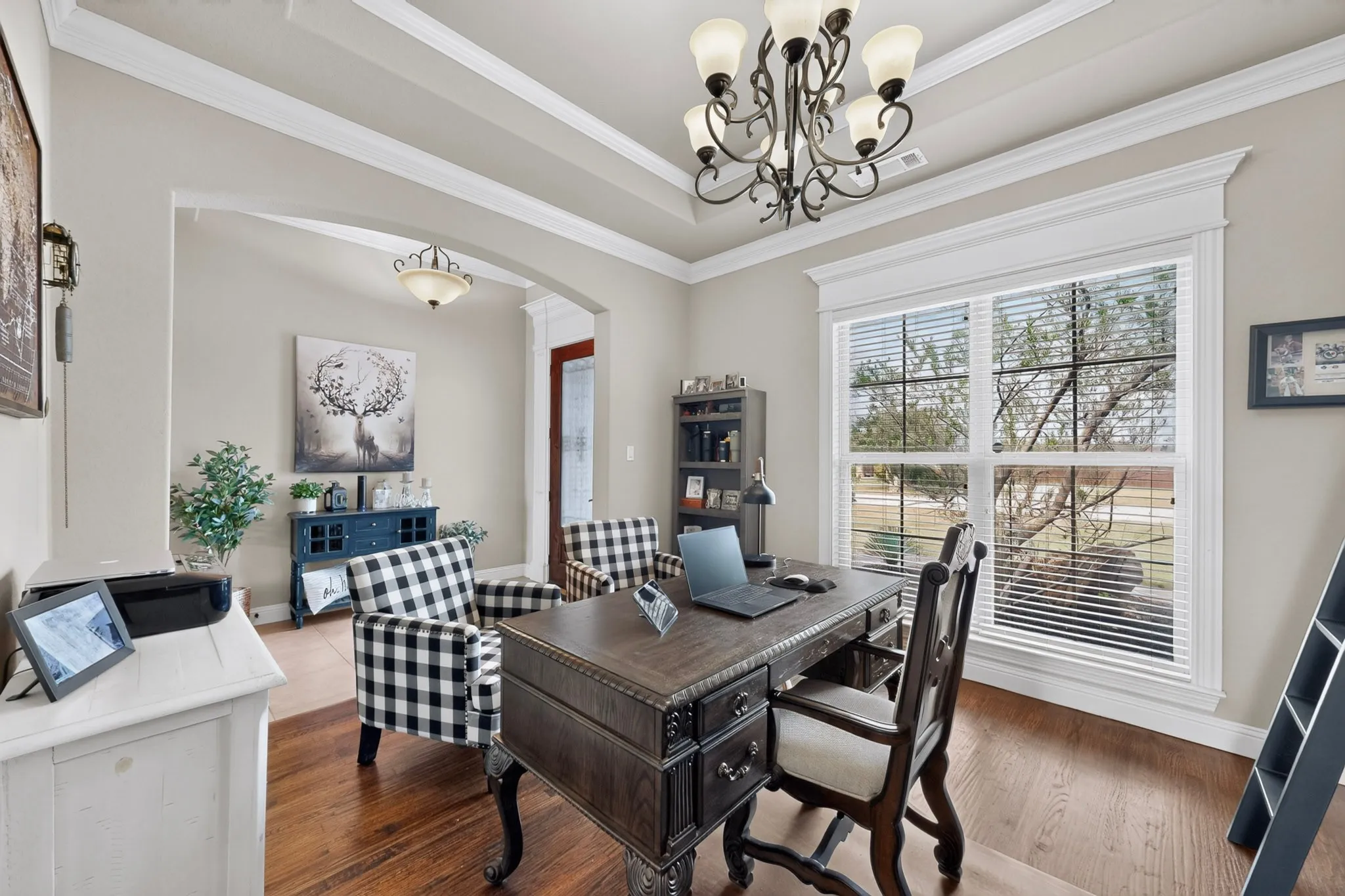 Hardwood-finish flooring, recessed tray ceiling with crown molding, decorative chandelier, arched entryway, and large windows with blinds