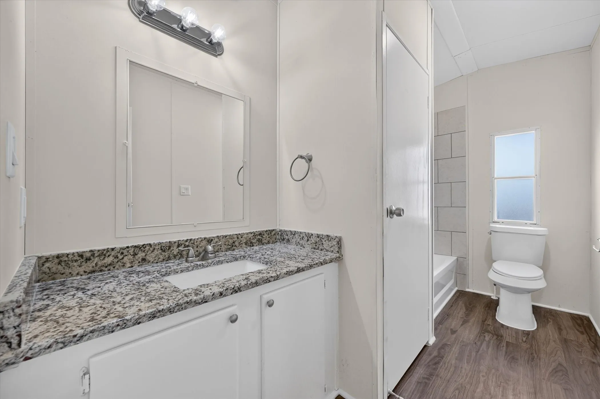 White vanity with a granite-style countertop and integrated sink, chrome faucet, and overhead vanity lighting