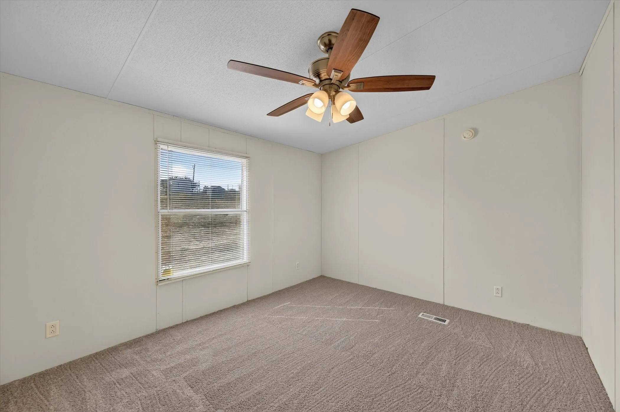 Neutral tone wall paneling with a window, ceiling fan with integrated lighting, and carpeted flooring