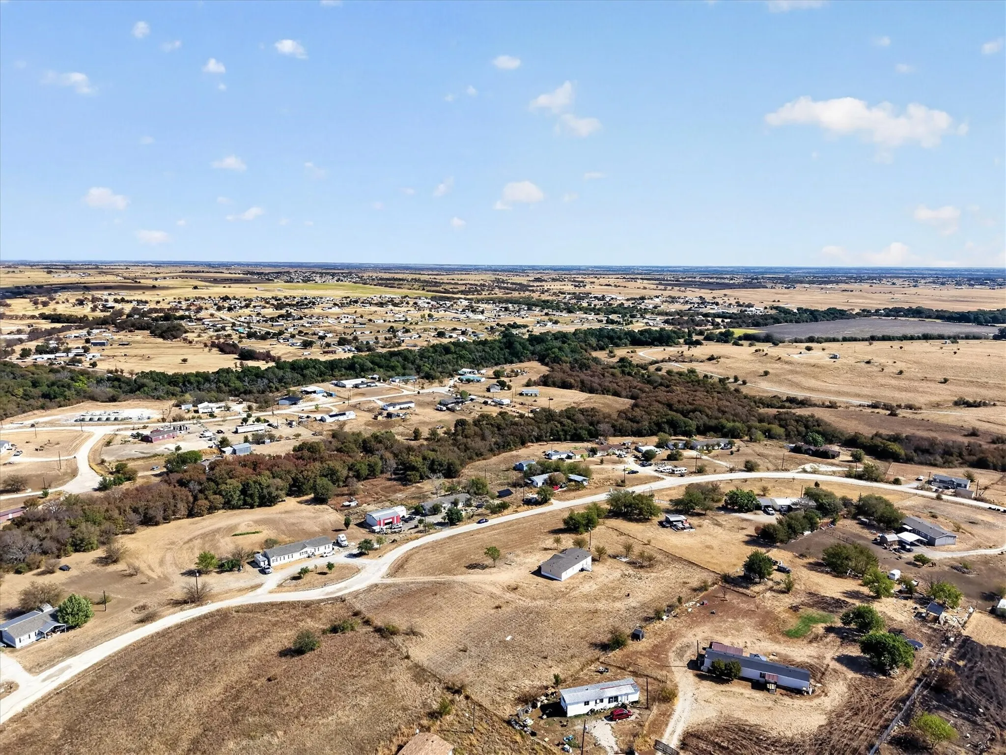 Expansive rural landscape featuring scattered residential structures, mature trees, and unpaved roads