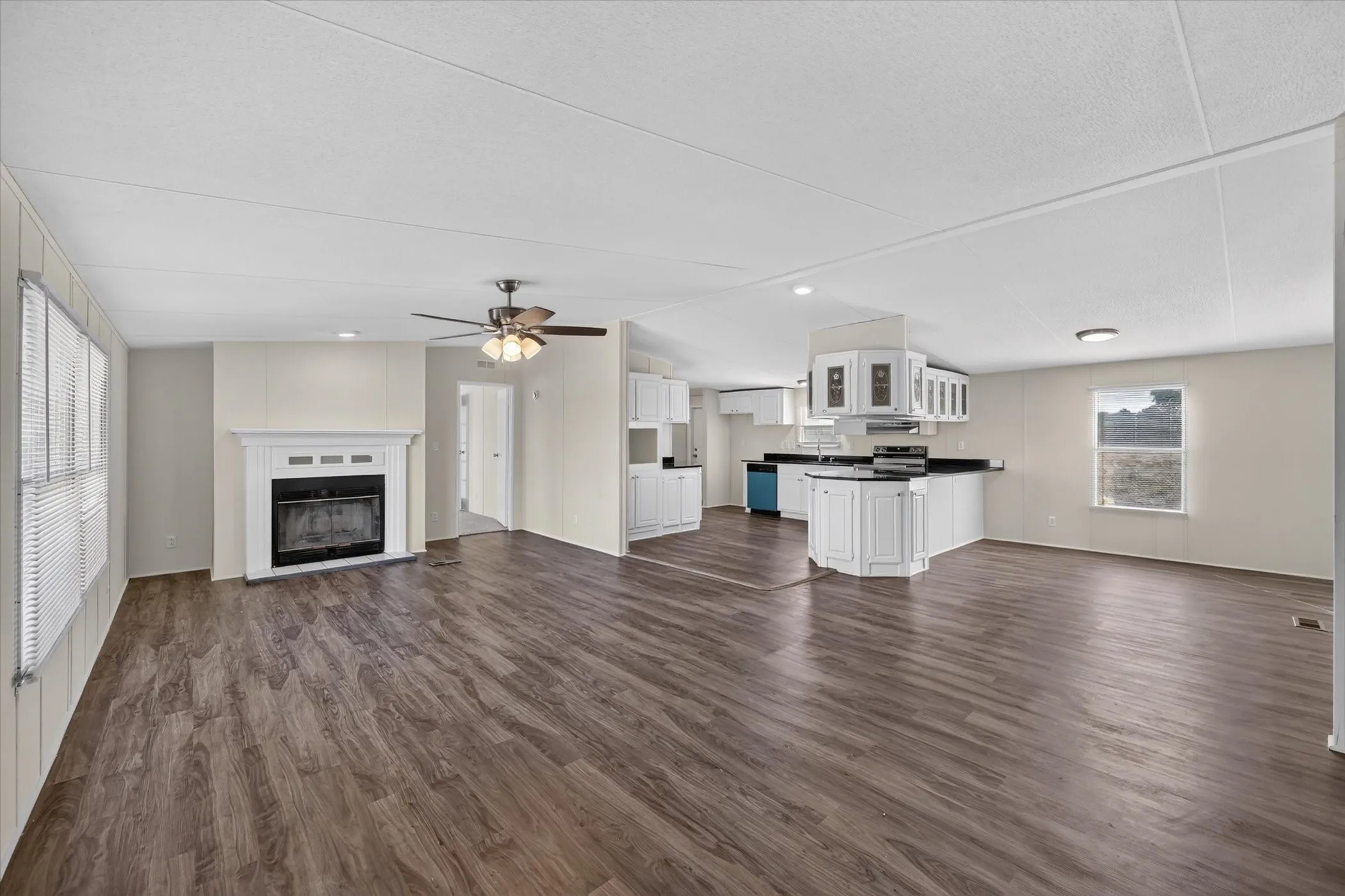 Open-concept living area with wood-finish flooring, a white mantel fireplace, and a ceiling fan