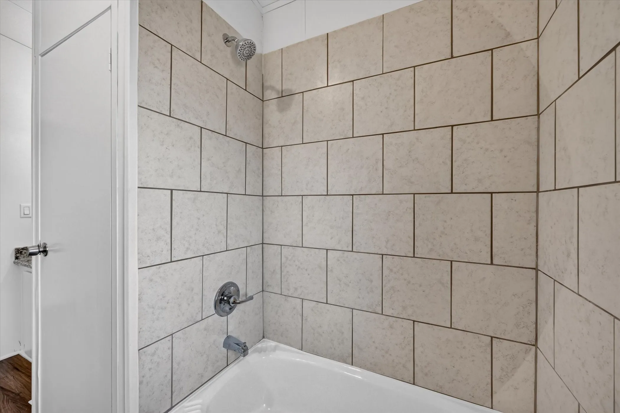 White bathtub with a chrome showerhead and faucet, surrounded by light-toned rectangular wall tiles