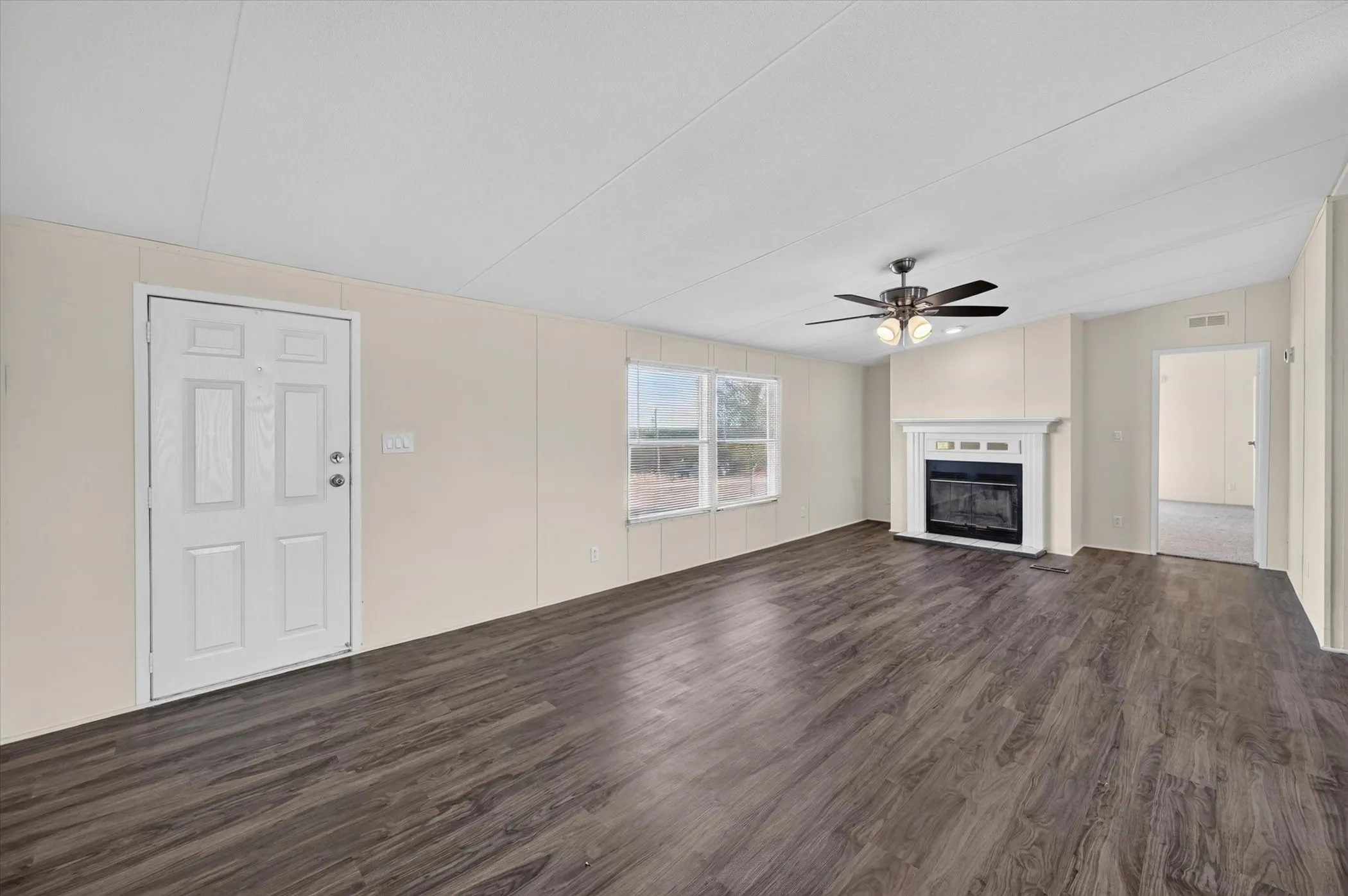 Expansive open-concept living area featuring wood-finish flooring, a decorative fireplace with a mantel, multiple windows, and a ceiling fan with integrated lighting