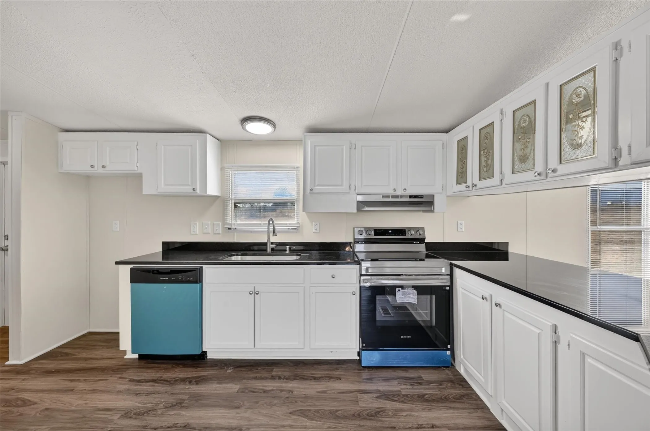 Kitchen featuring wood-finish flooring, white cabinetry, dark countertops, a window, and a stainless steel oven