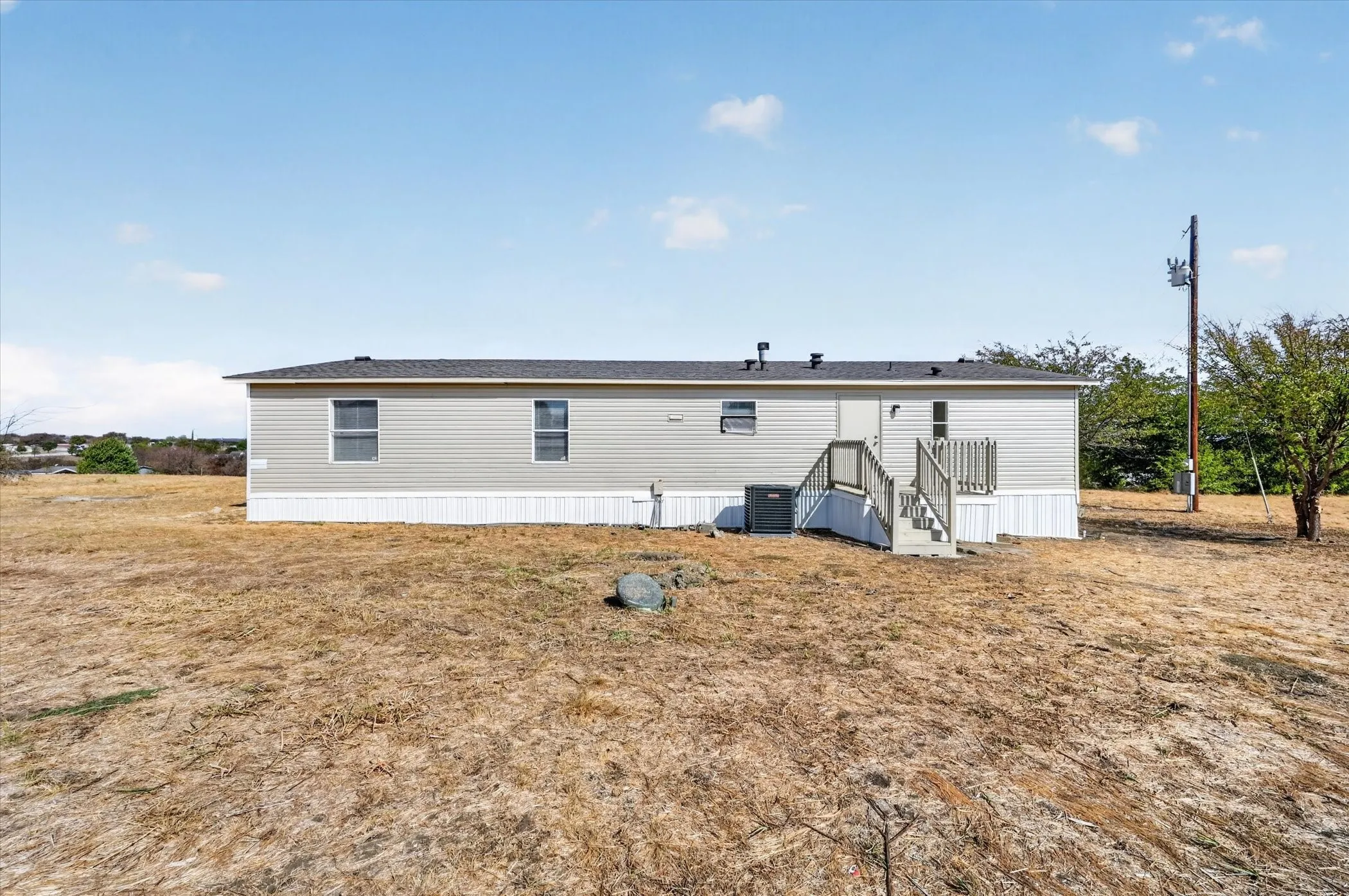 Manufactured residence with light gray siding, dark shingle roof, and white skirting