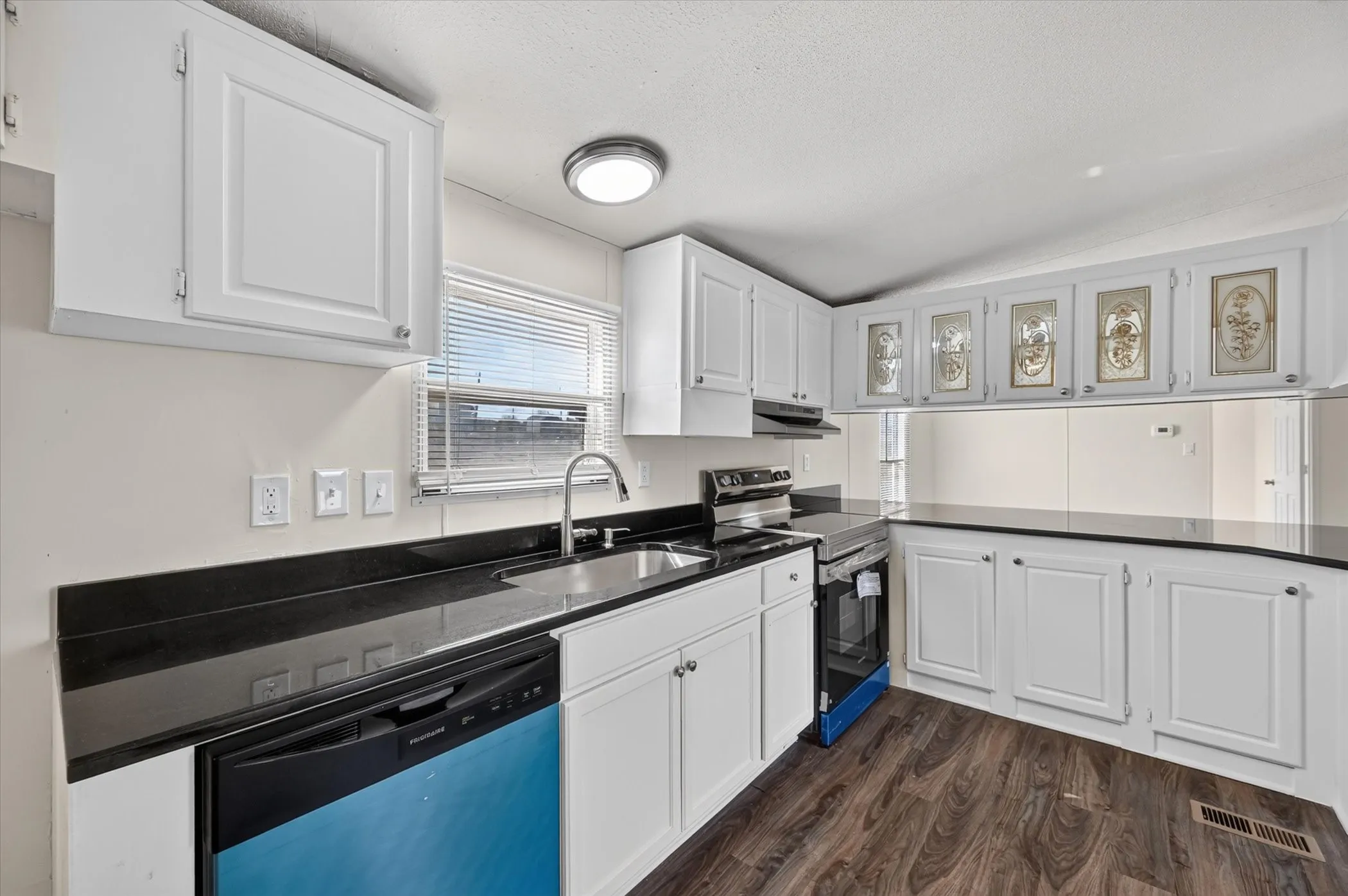 Kitchen featuring white cabinetry, dark countertops, wood-finish flooring, and stainless steel appliances