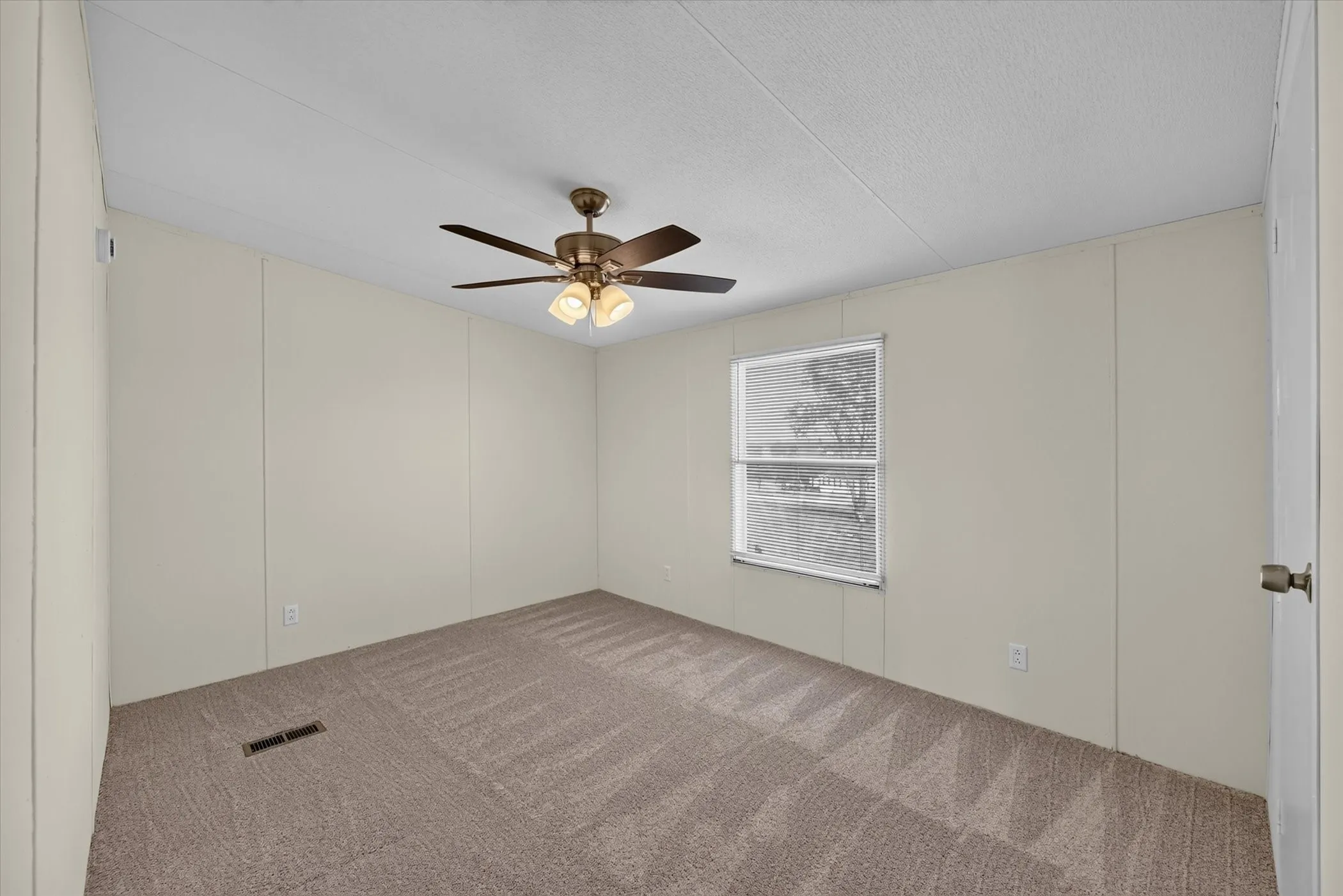 Carpeted room with a ceiling fan, light-colored walls, and a window providing natural illumination
