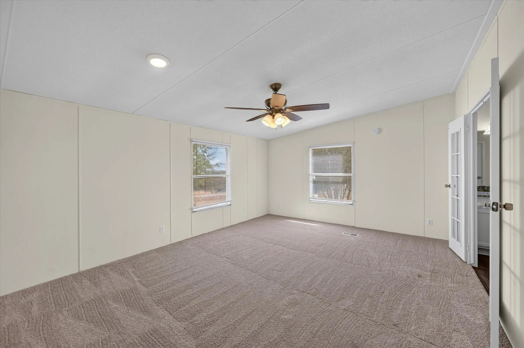 Spacious room featuring sloped ceilings, two windows, wall-to-wall carpeting, and a ceiling fan with integrated lighting
