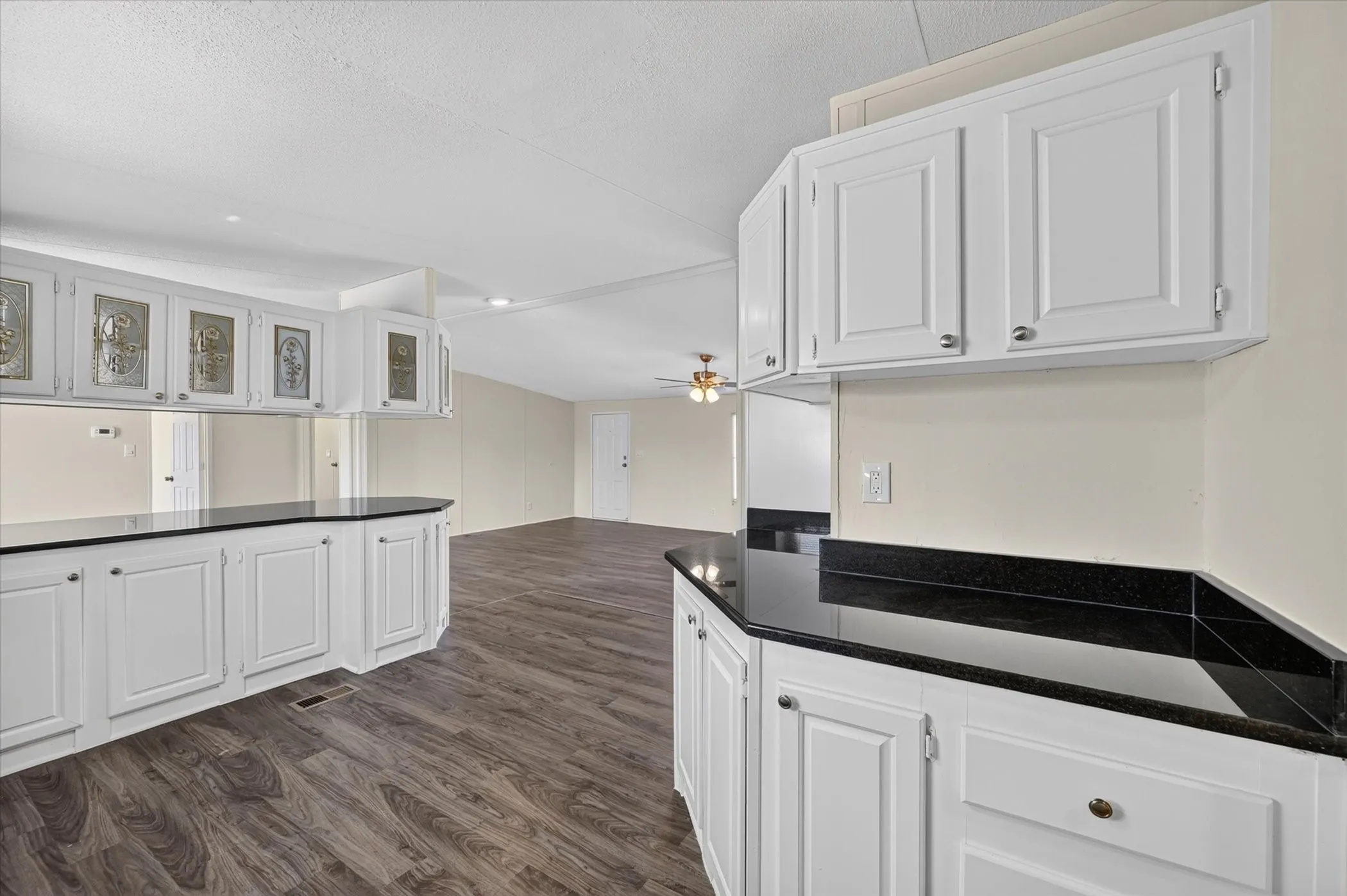 Extensive white cabinetry with varied door styles, dark countertops, and wood-finish flooring