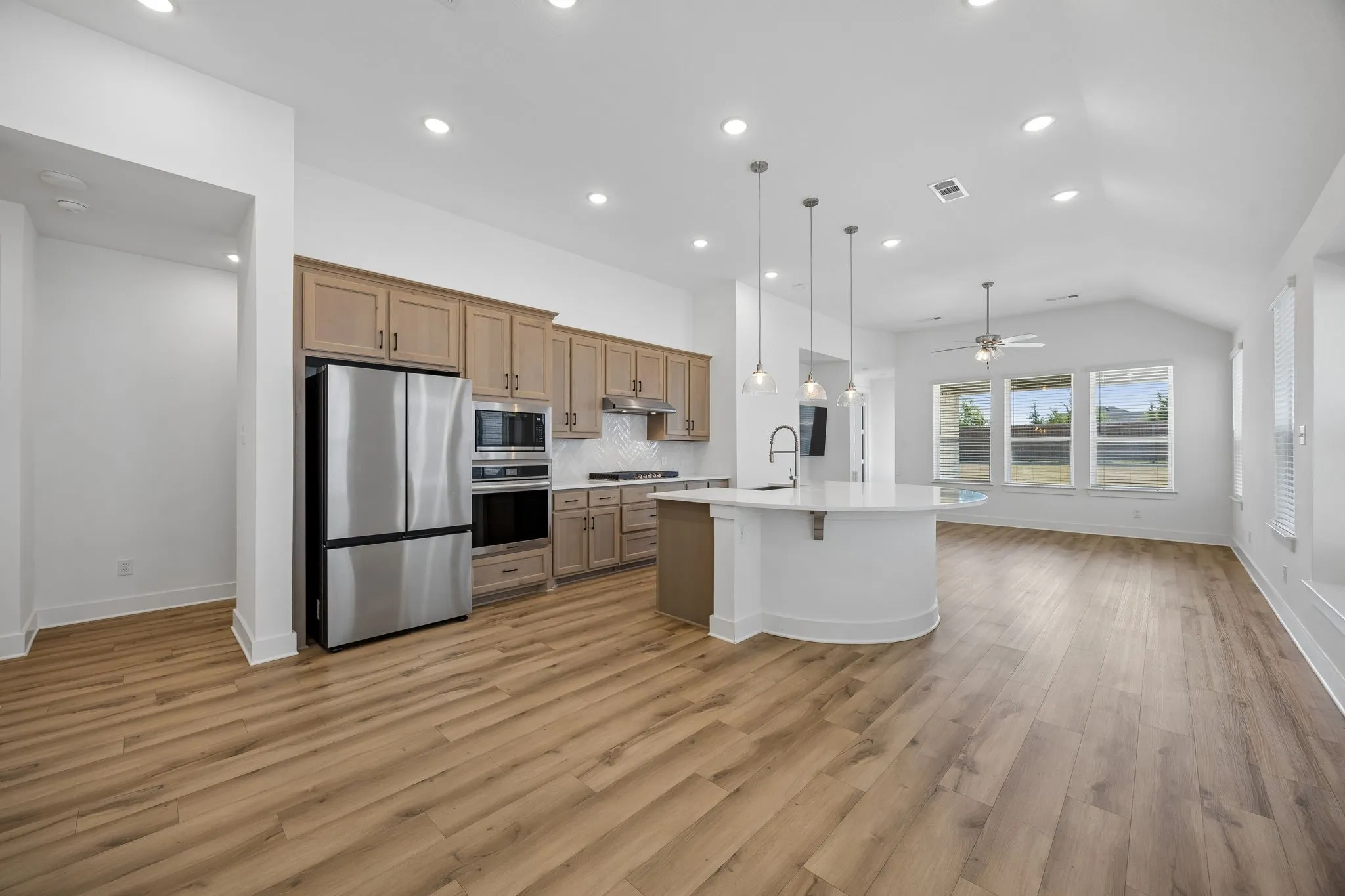 Open-concept living area with wood-finish flooring, recessed lighting, and a vaulted ceiling