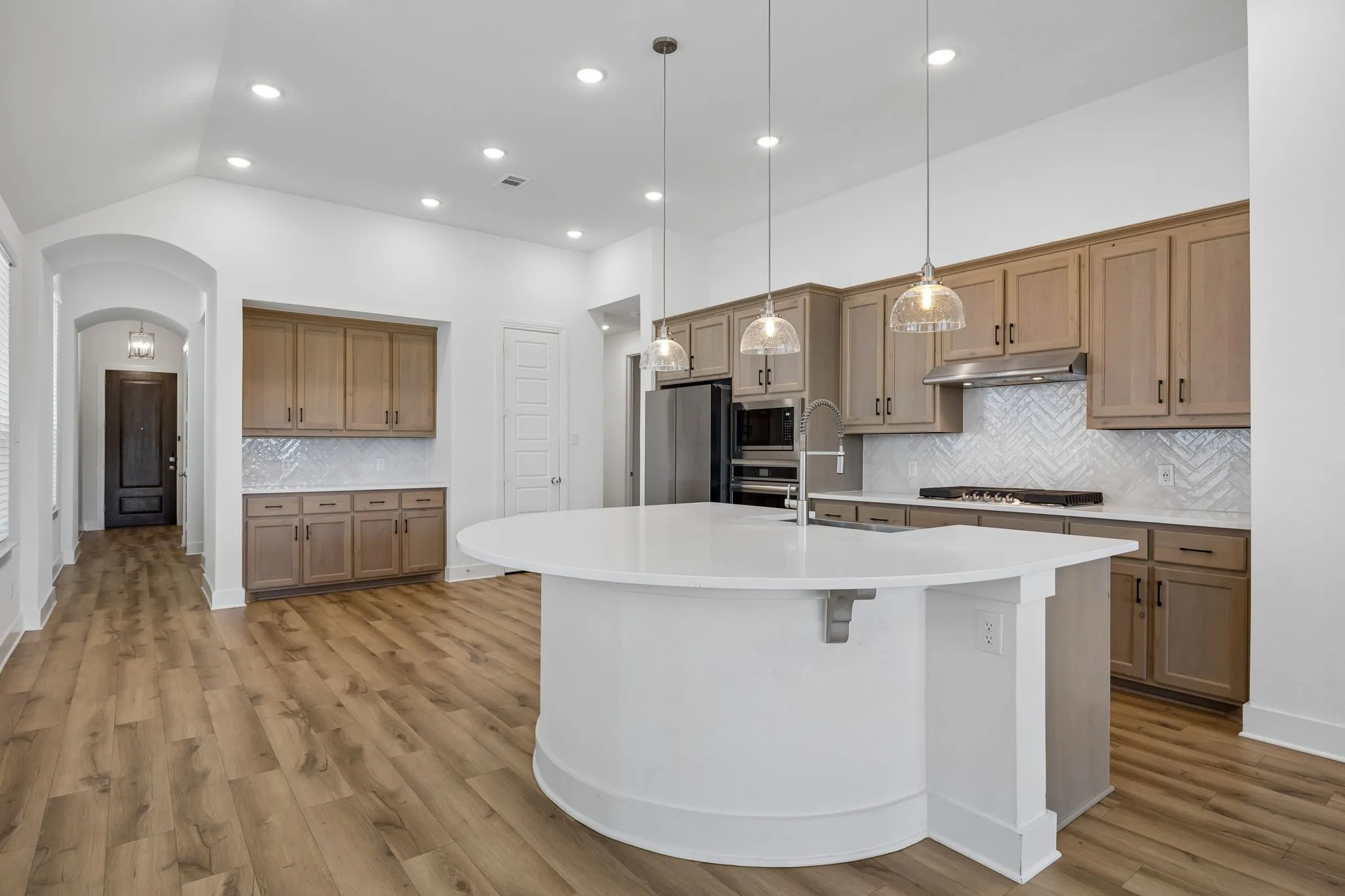 Kitchen featuring wood-finish cabinetry, stainless steel appliances, a herringbone tile backsplash, and a large central island with a solid surface countertop