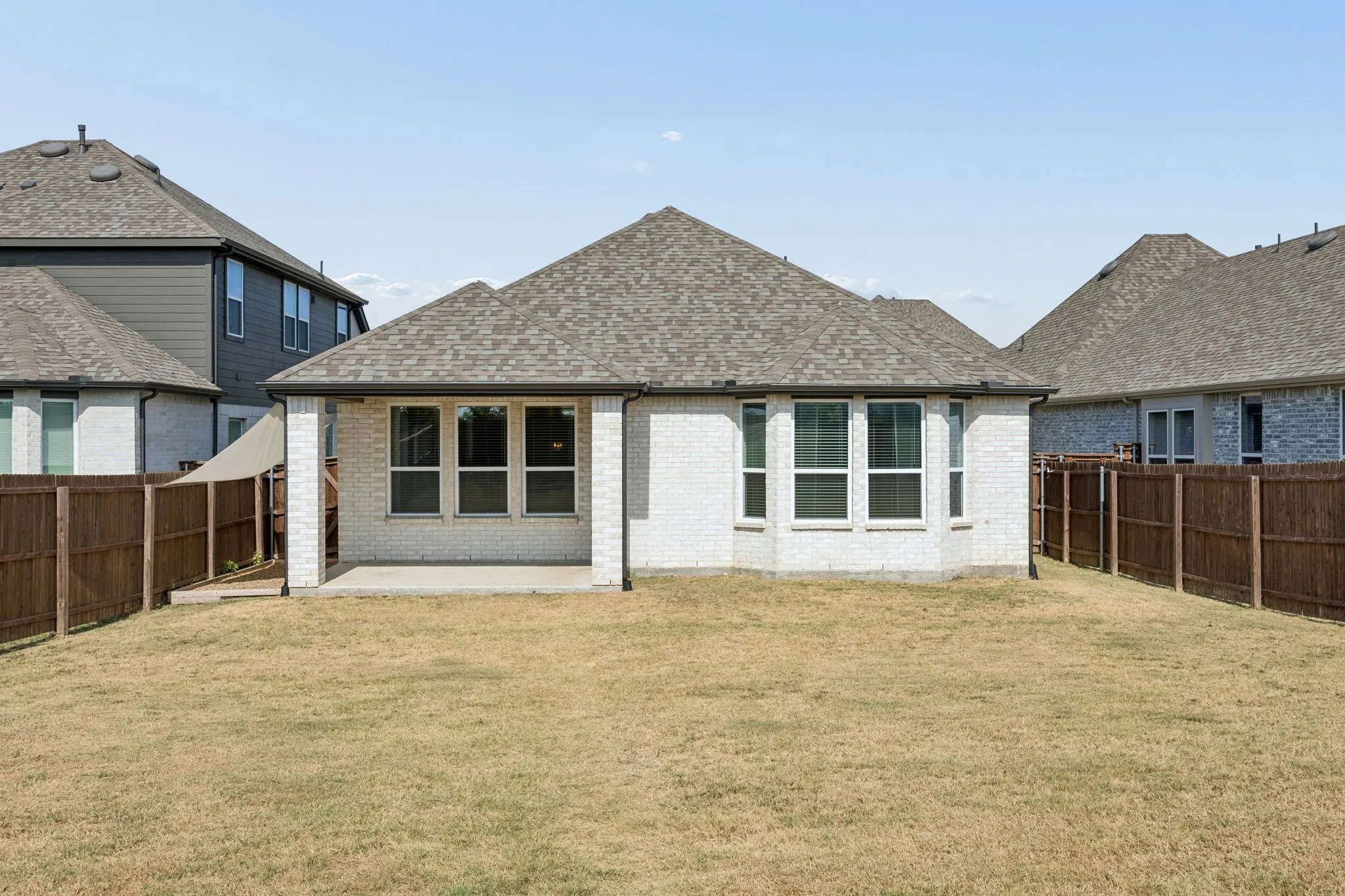Expansive backyard featuring a covered patio, full brick exterior, and a privacy fence