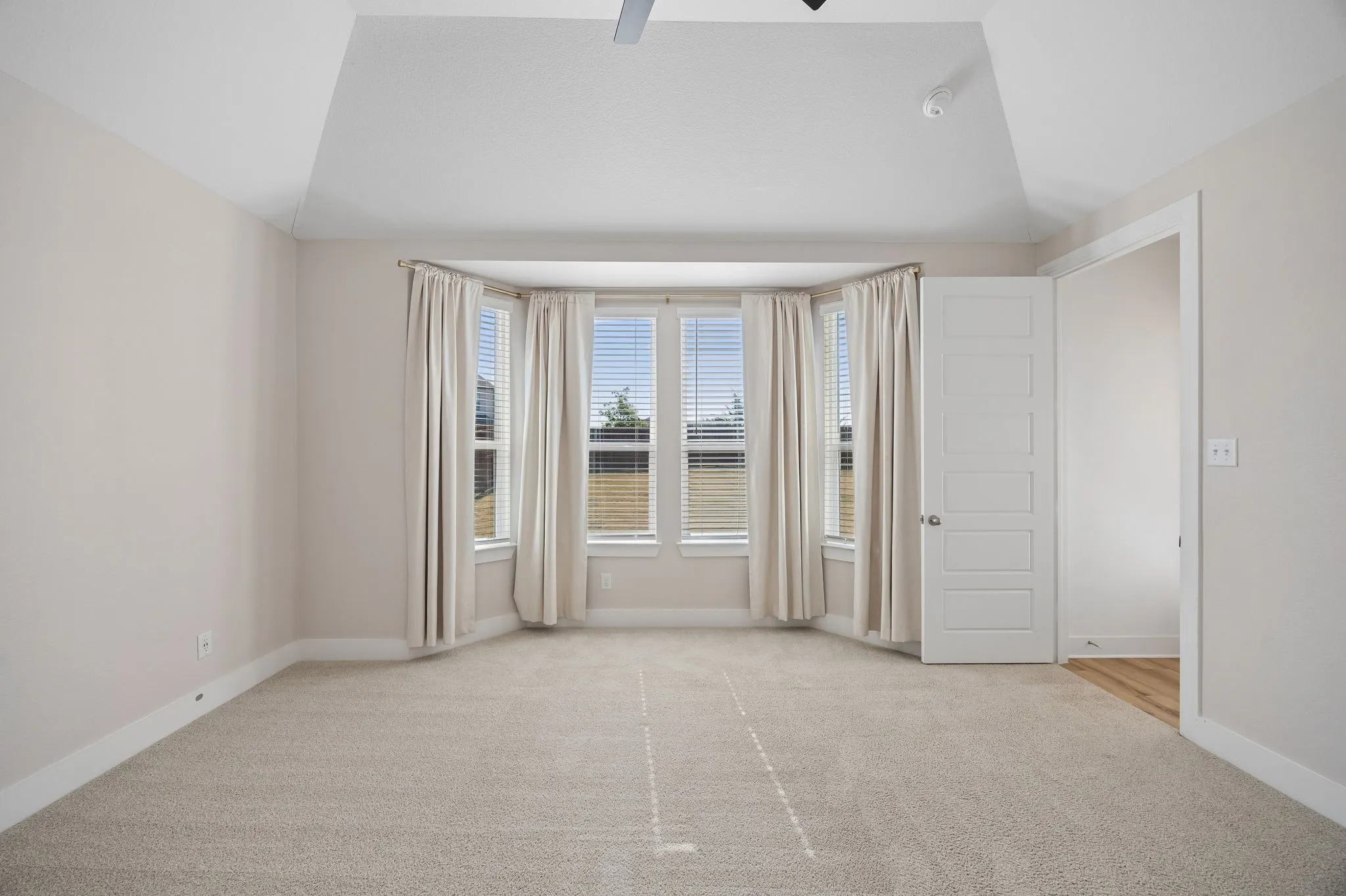 Primary Bedroom Vaulted ceiling with fan, bay window with blinds, light-colored carpeting, white trim, and a five-panel interior door