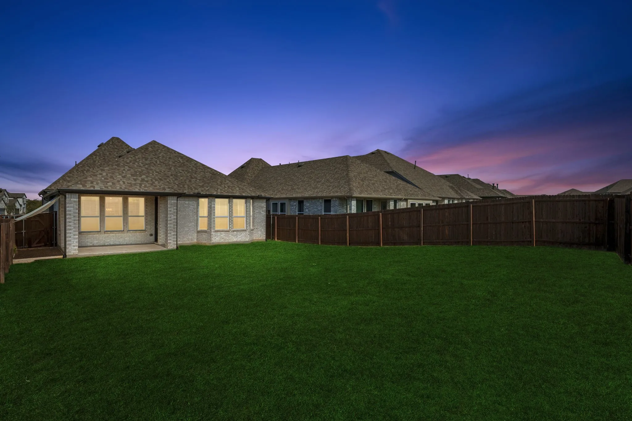 Expansive green lawn, covered patio, brick exterior, multiple windows, and a wood privacy fence
