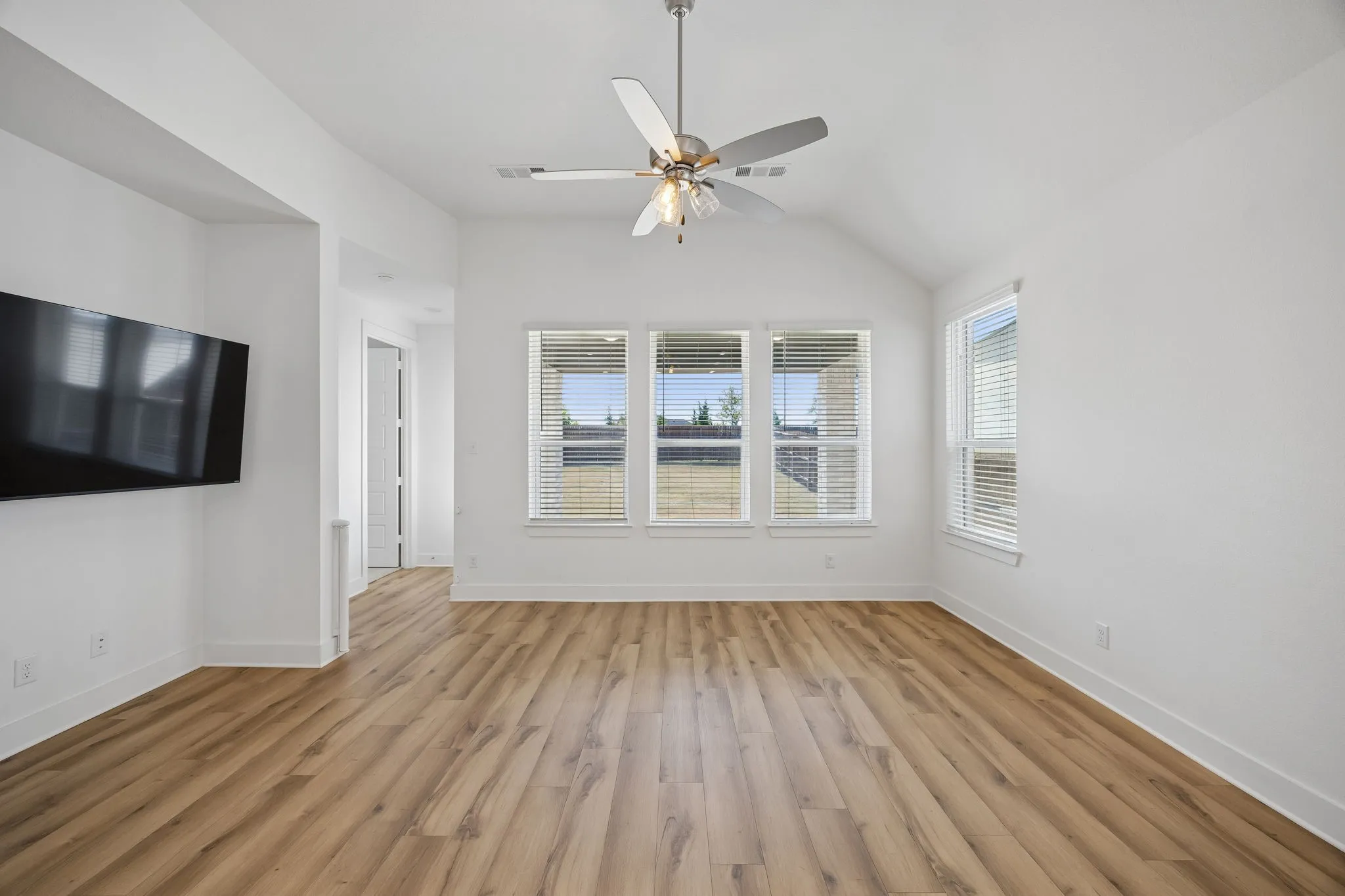 Vaulted ceiling with an attached ceiling fan, bay window with blinds, light-toned carpet, and a paneled door