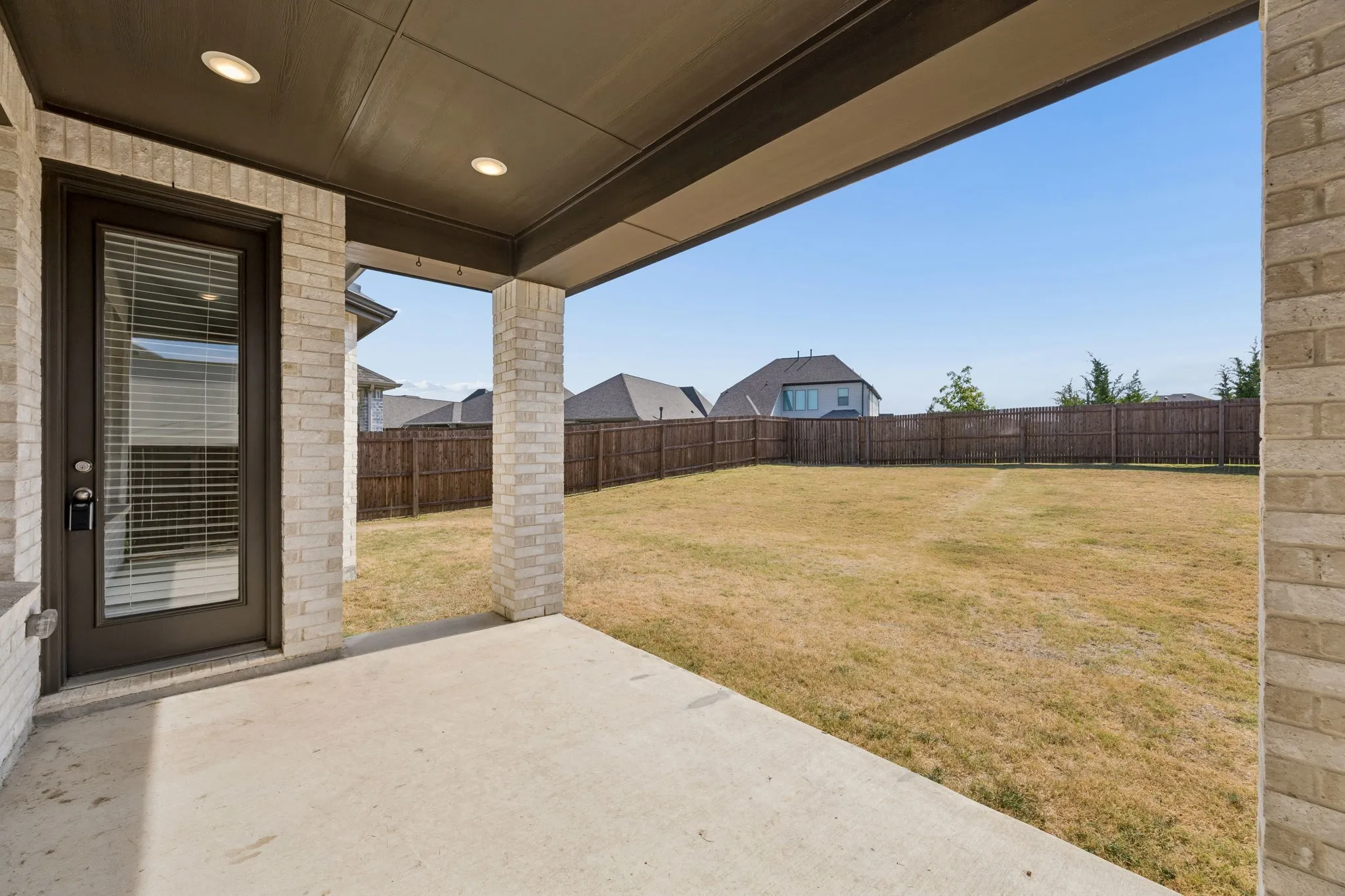 Expansive yard with wood fencing, a stone patio, and multiple windows across the rear elevation