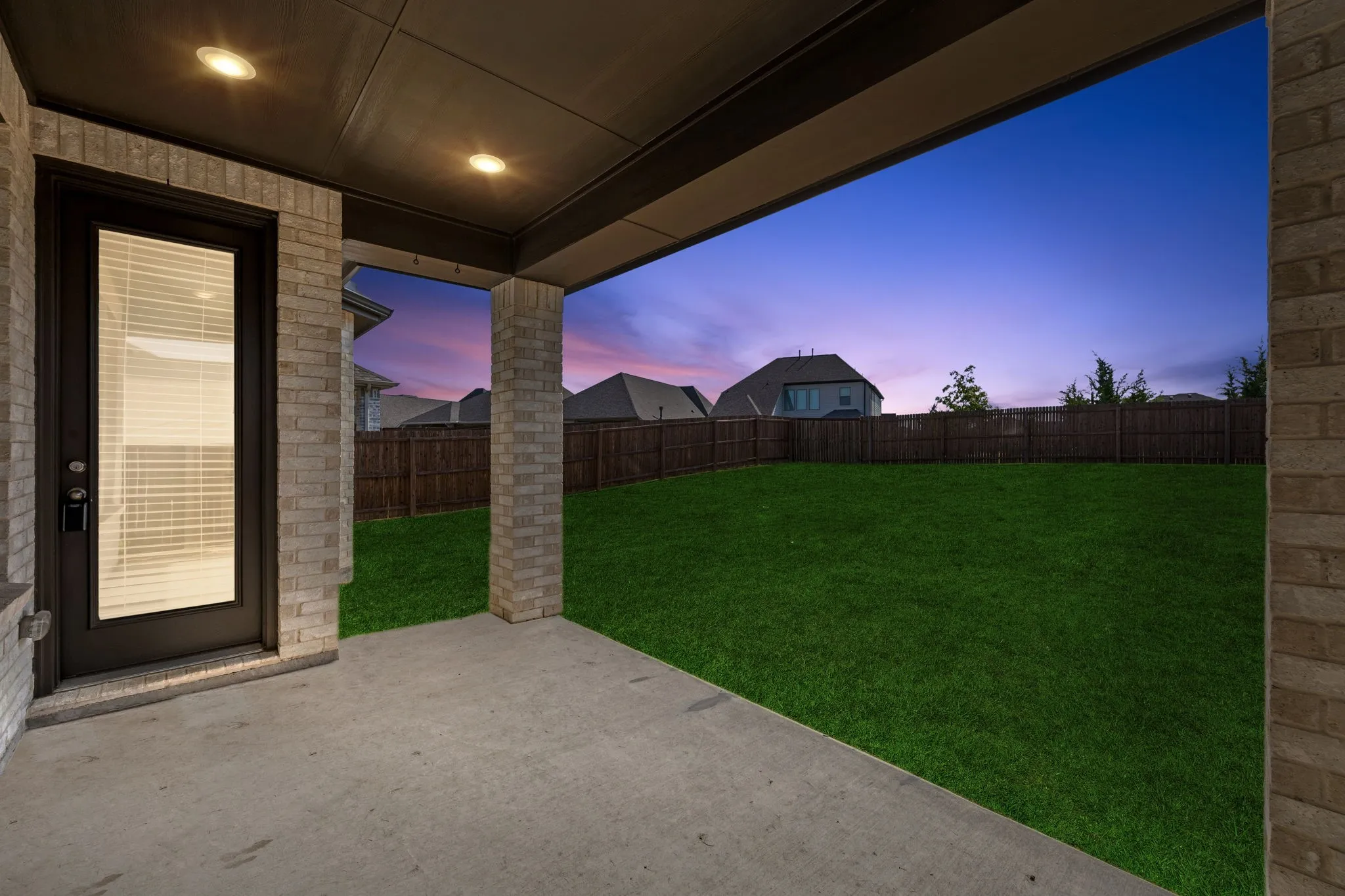 Expansive backyard featuring a large green lawn, full privacy fencing, and a concrete patio