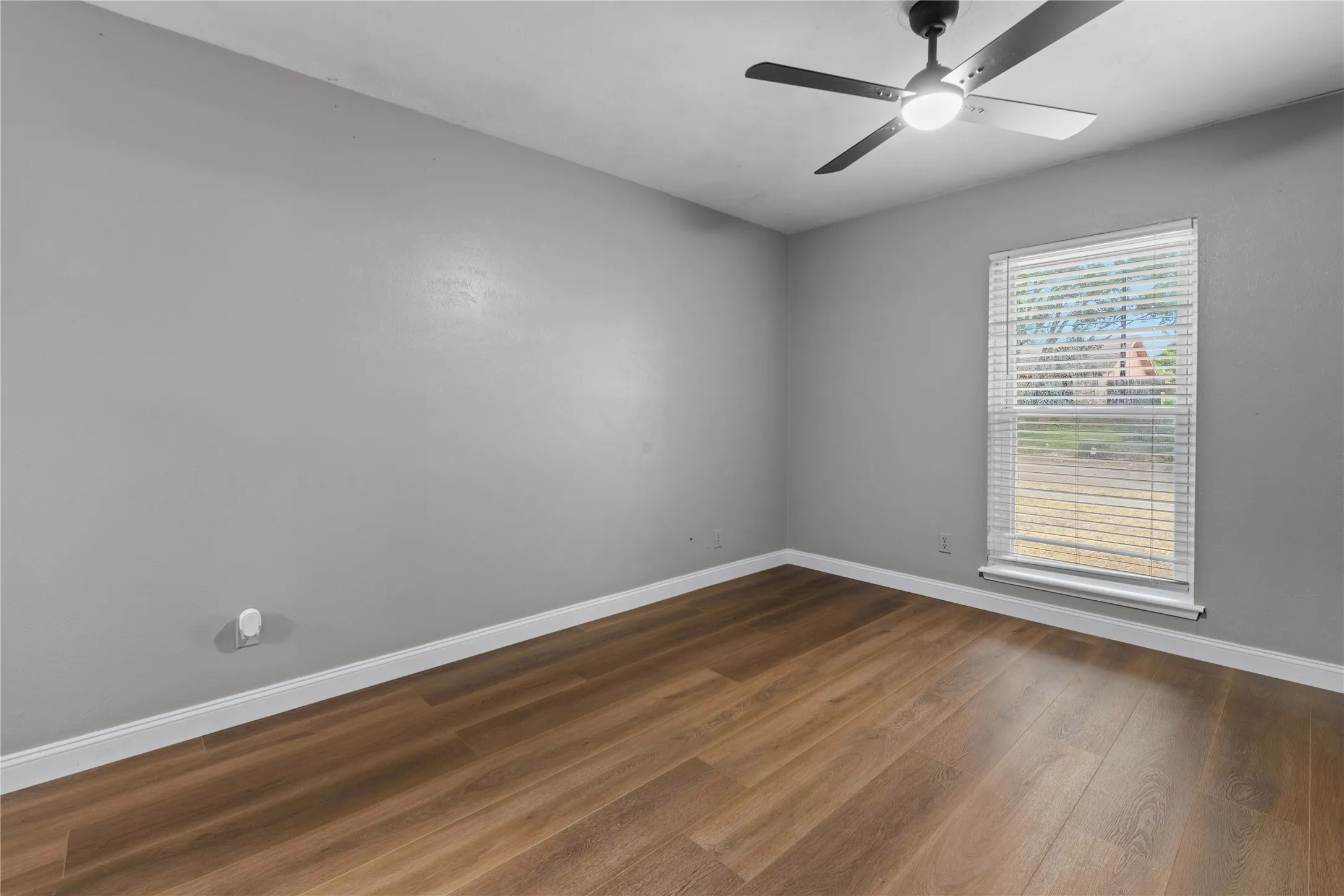 Wood-finish flooring, neutral gray walls, white trim, and a ceiling fan with integrated lighting