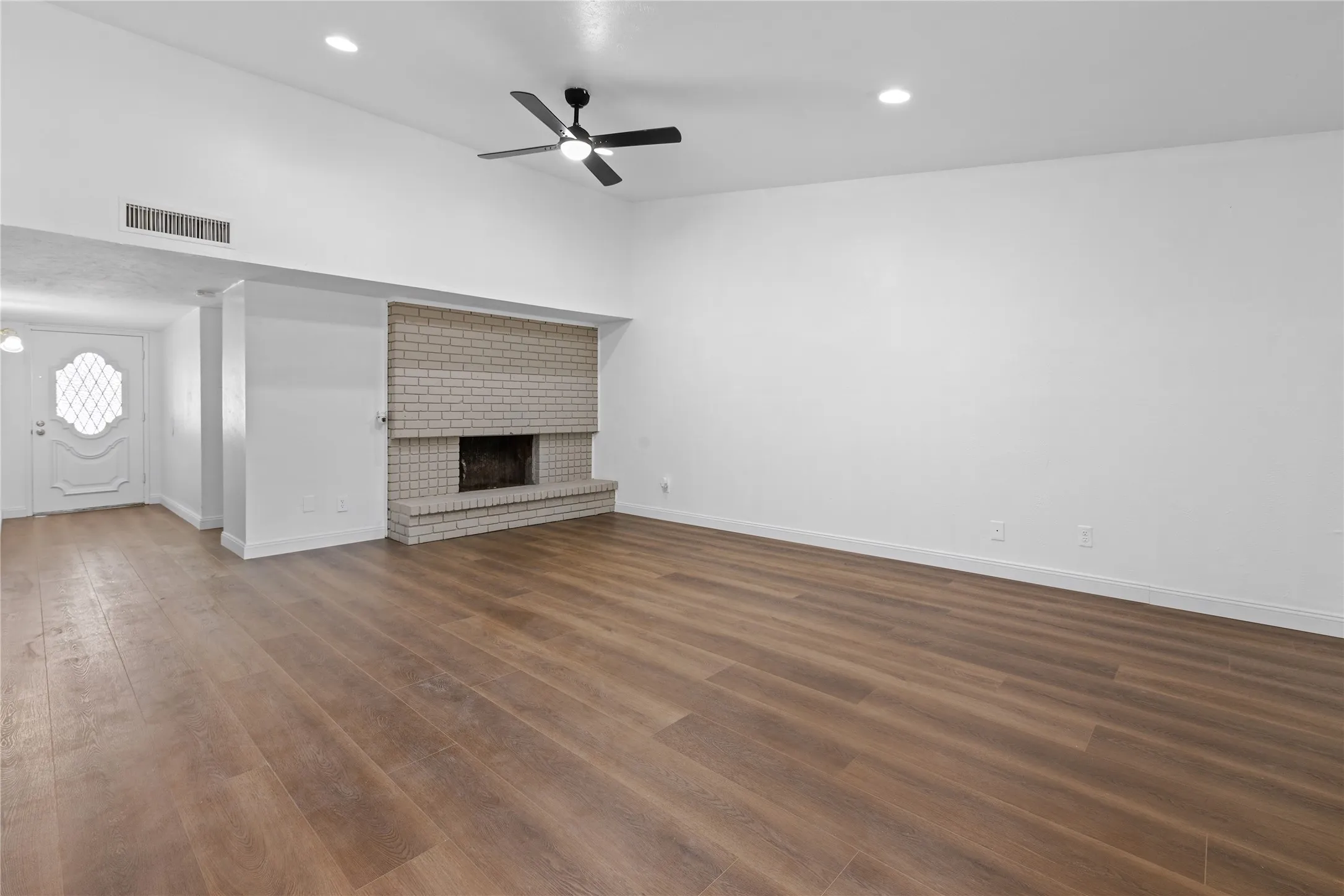 Vaulted ceiling with a ceiling fan, wood-finish flooring, recessed lighting, and a brick fireplace