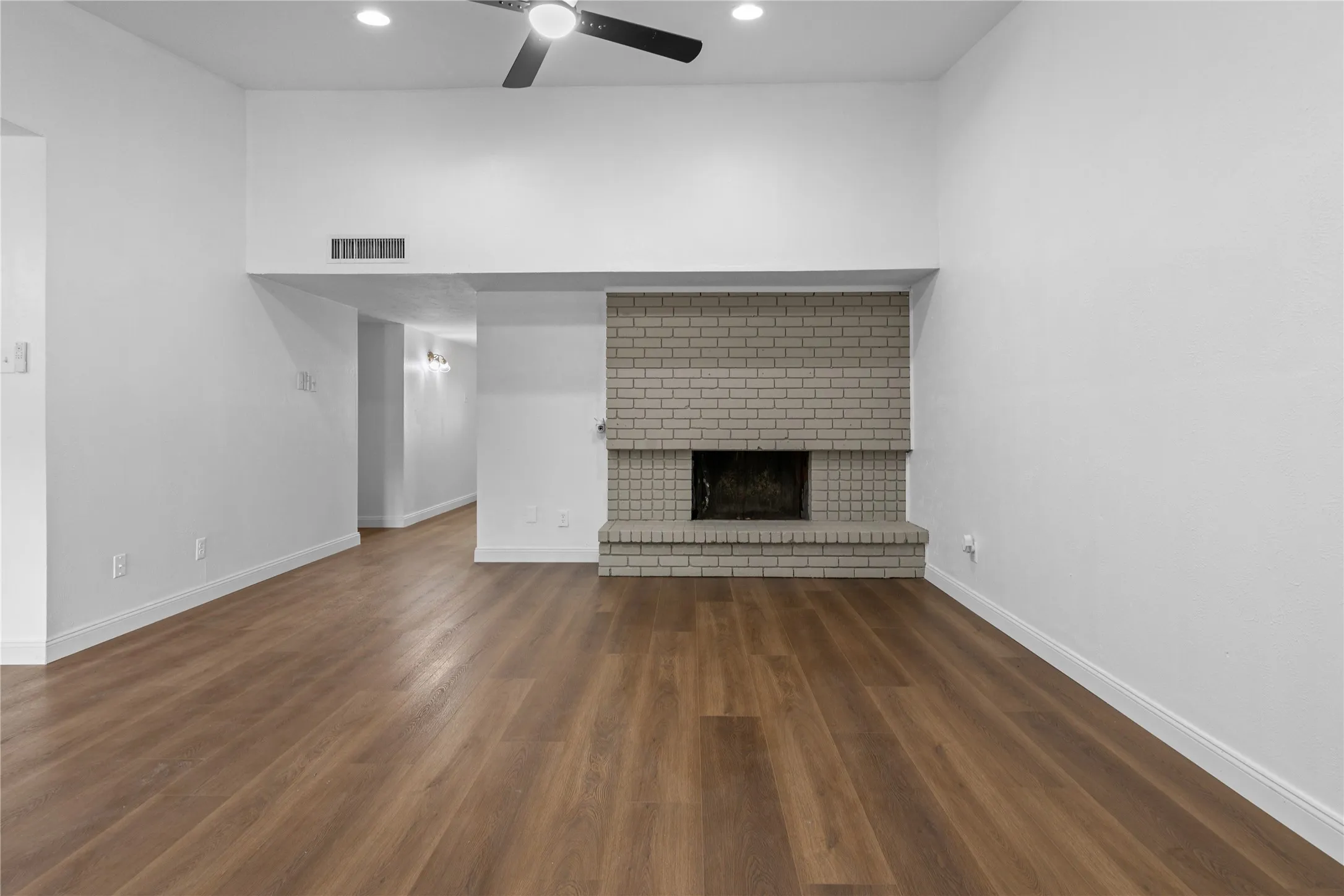 Expansive living area featuring wood-finish flooring, a painted brick fireplace, a ceiling fan, and recessed lighting