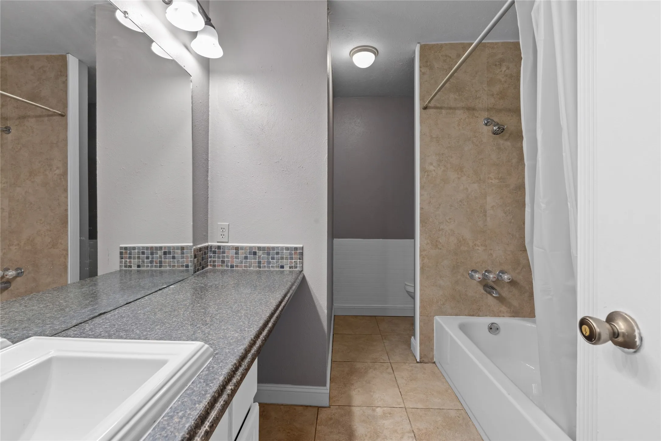 Bathroom featuring a vanity with an integrated sink, a full-width mirror, tile backsplash, and a tiled shower/tub combination