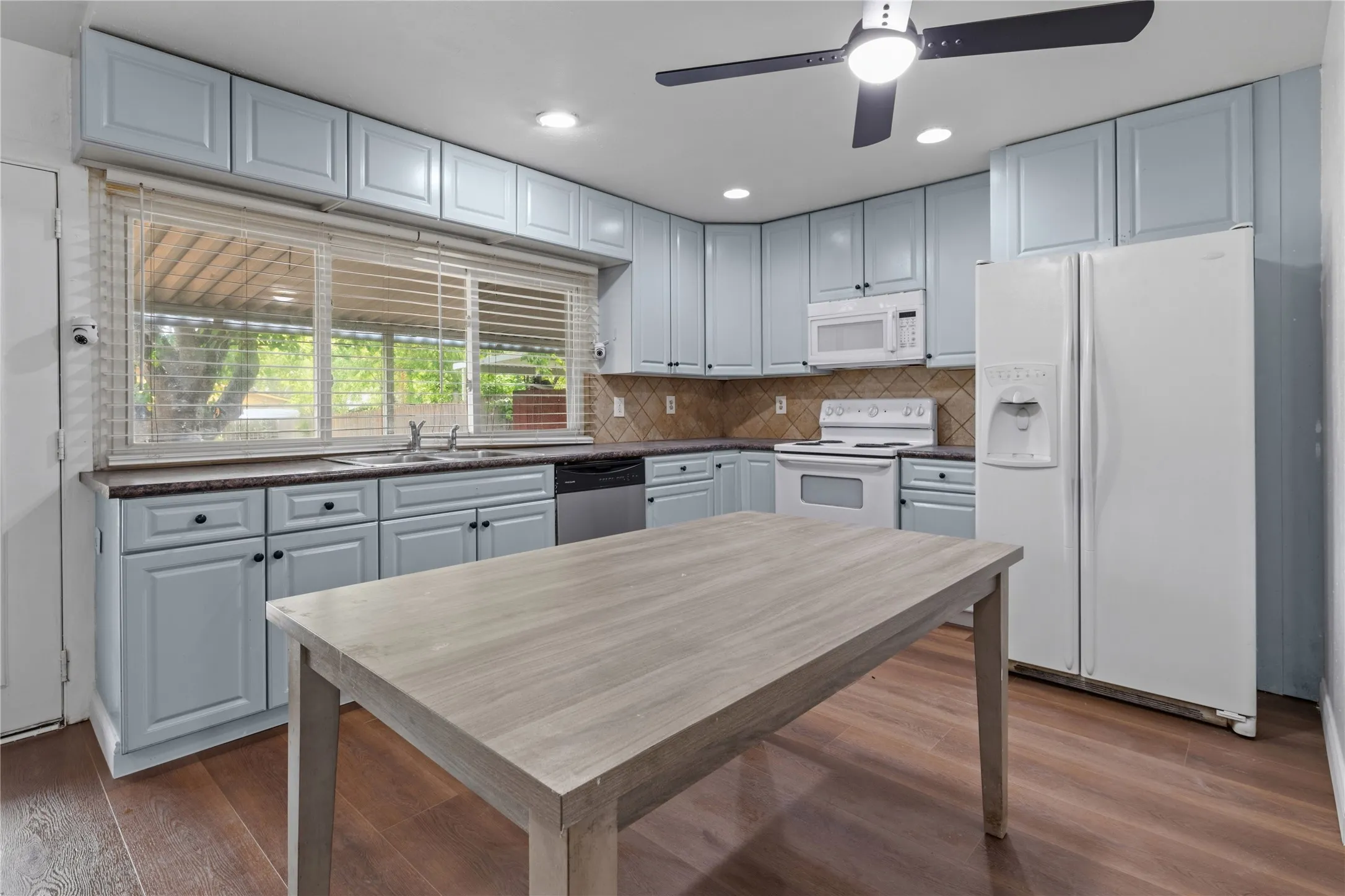 Kitchen featuring light blue cabinetry, dark countertops, a tile backsplash, and wood-finish flooring