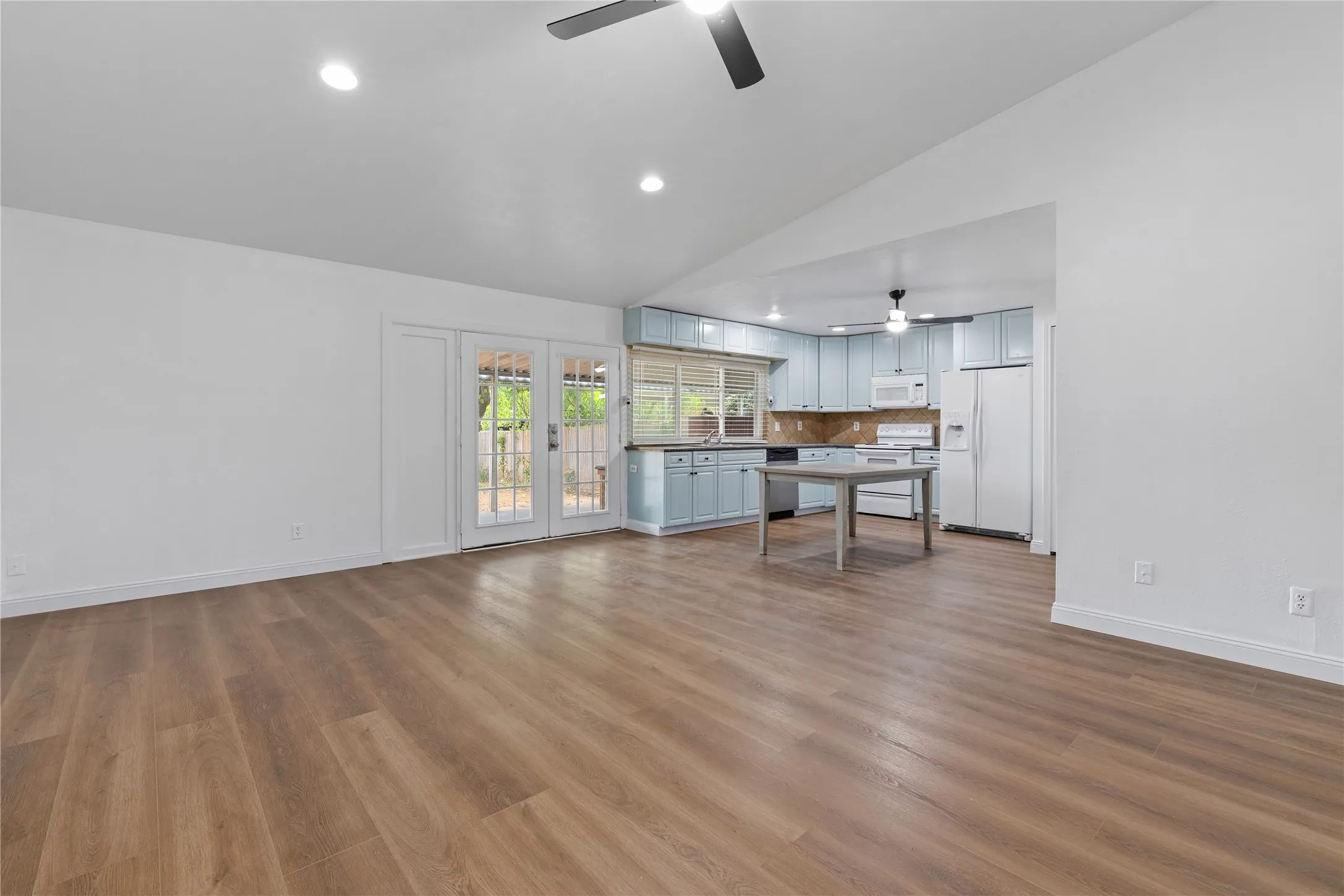 Vaulted ceiling, recessed lighting, wood-finish flooring, French doors, and a kitchen featuring light blue cabinetry and white appliances