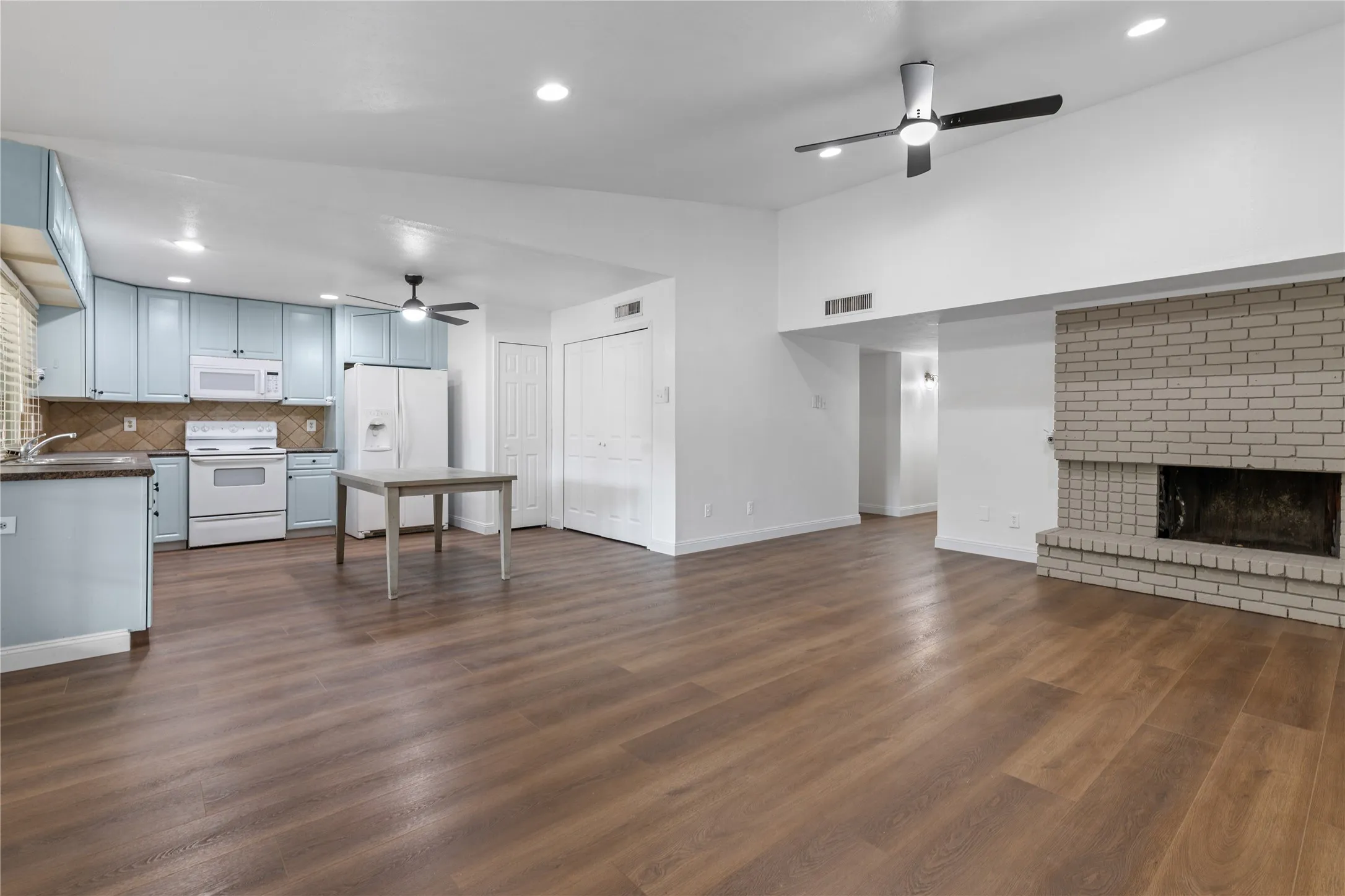 Open-concept living space featuring wood-finish flooring, a painted brick fireplace, recessed lighting, and a vaulted ceiling