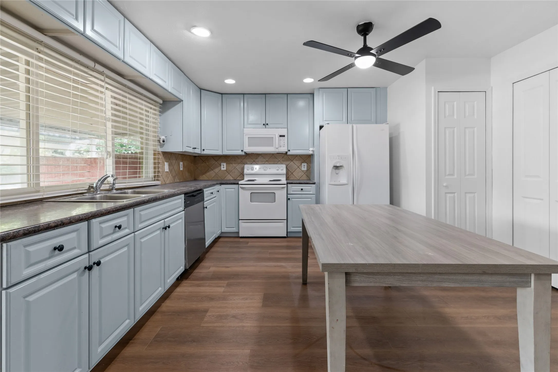 Bright kitchen featuring light blue cabinetry with hardware accents, white appliances, wood-finish countertops, and abundant natural light from multiple windows