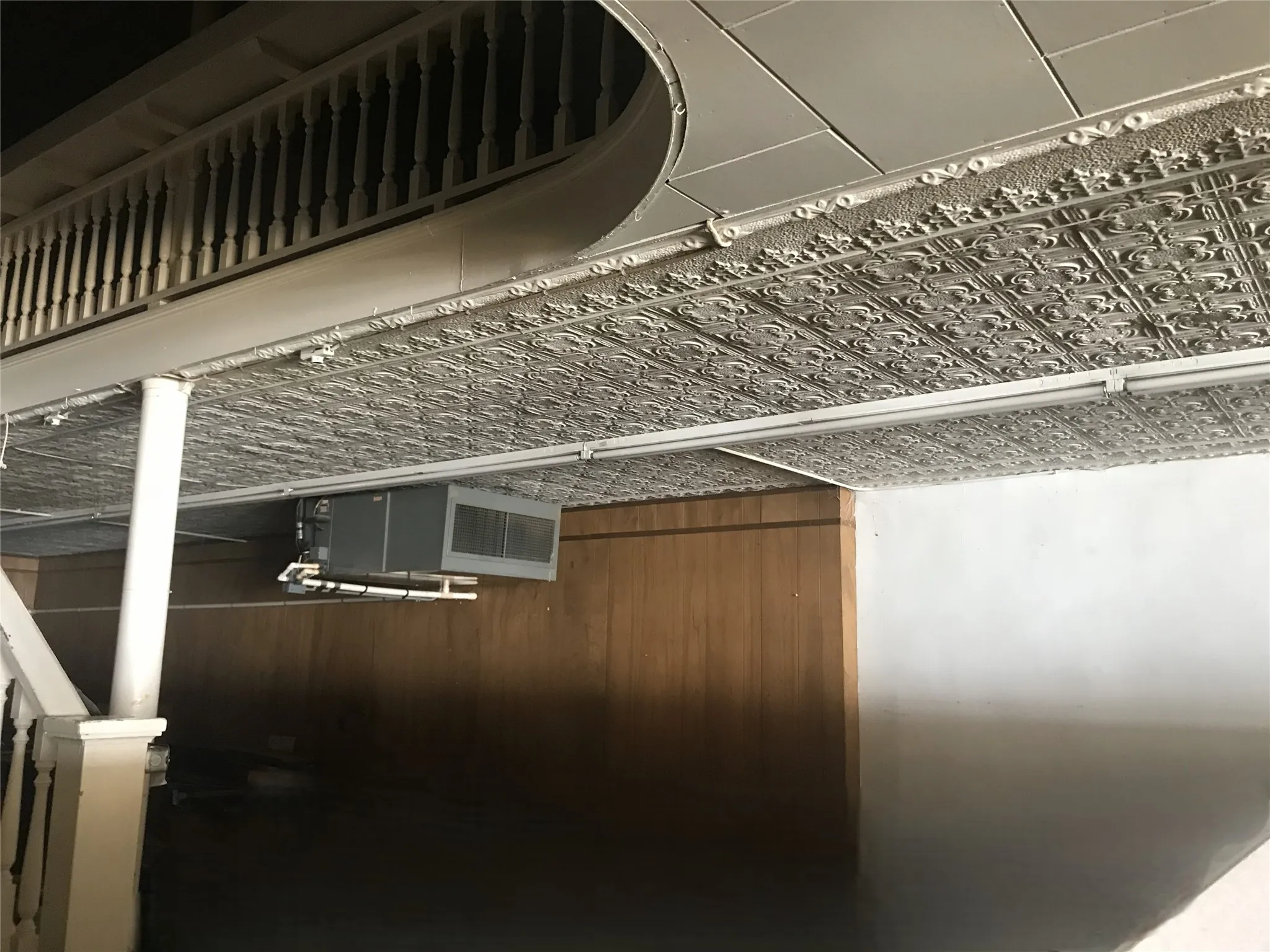 Decorative tin ceiling panels, wood-paneled walls, and a white balustrade