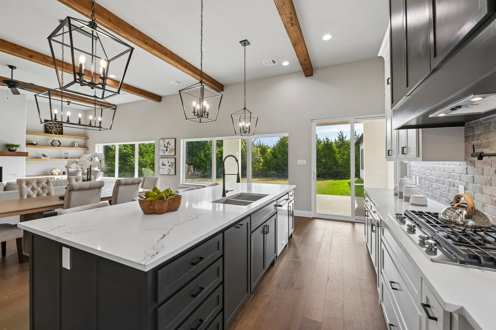 Open-concept kitchen with a large island, wood-finish flooring, exposed ceiling beams, and a sliding glass door leading to the exterior