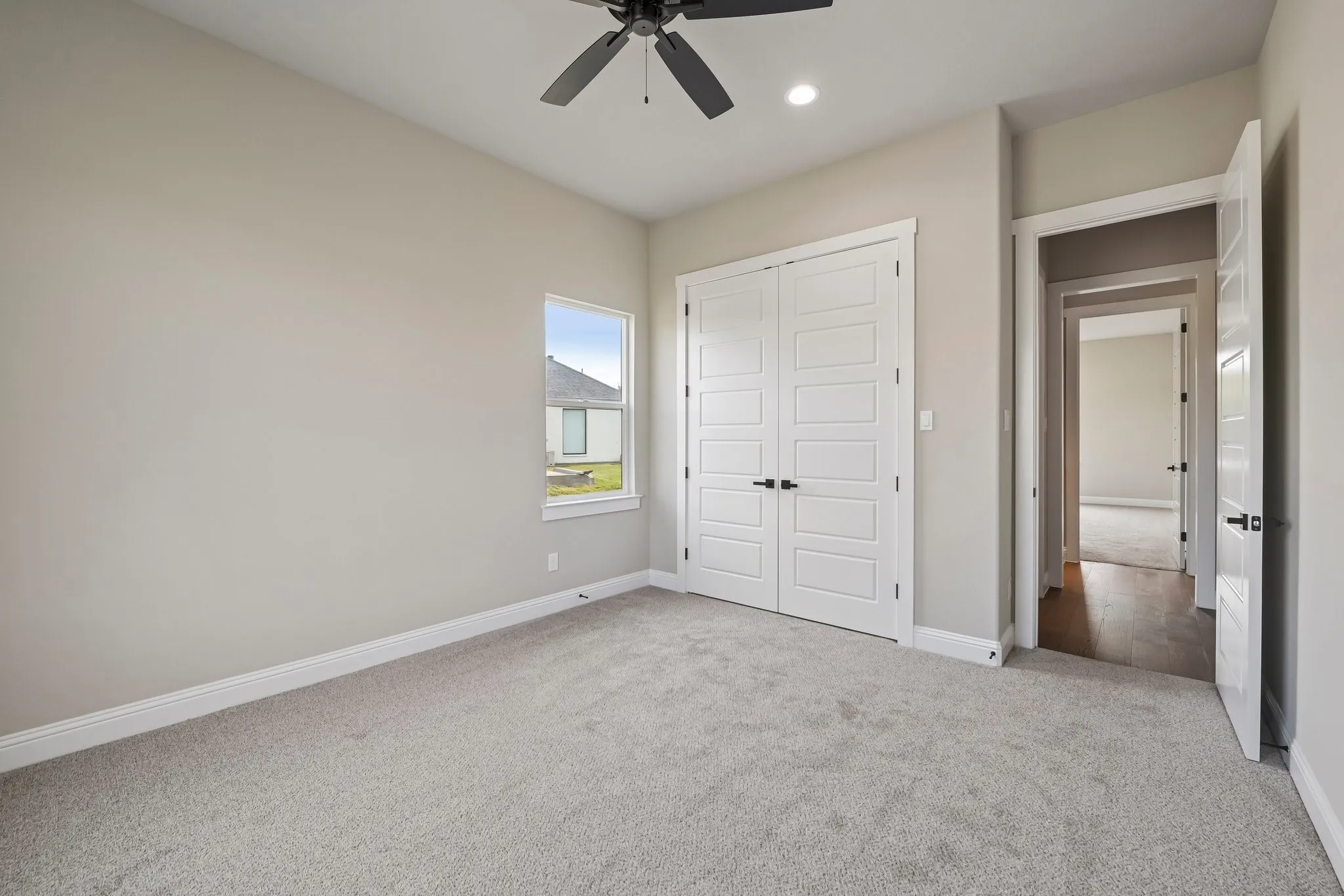 Carpeted flooring, contemporary ceiling fan, recessed lighting, double panel doors with black hardware, and a window providing natural light