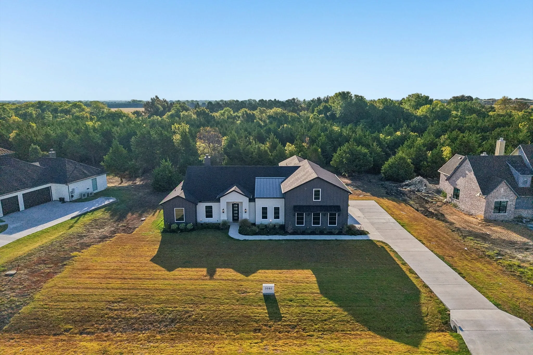 Modern farmhouse-style residence with a dark-pitched roof, contrasting light and dark siding, and a concrete driveway