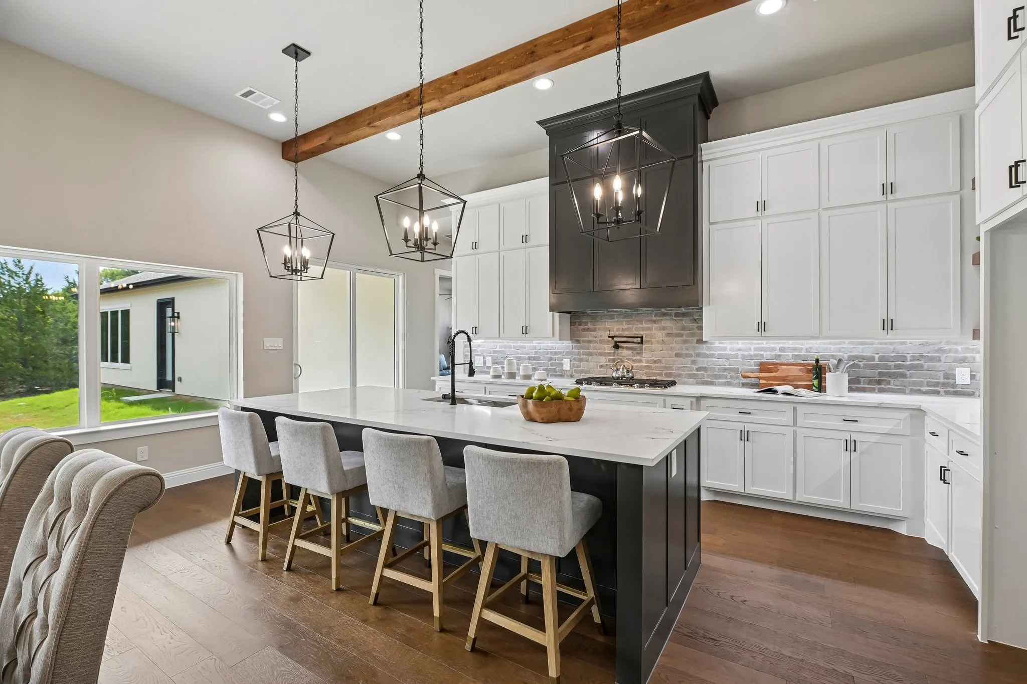 Kitchen with wood-finish flooring, white cabinetry, a large kitchen island with a light-toned countertop, a dark-toned range hood, and pendant lighting fixtures