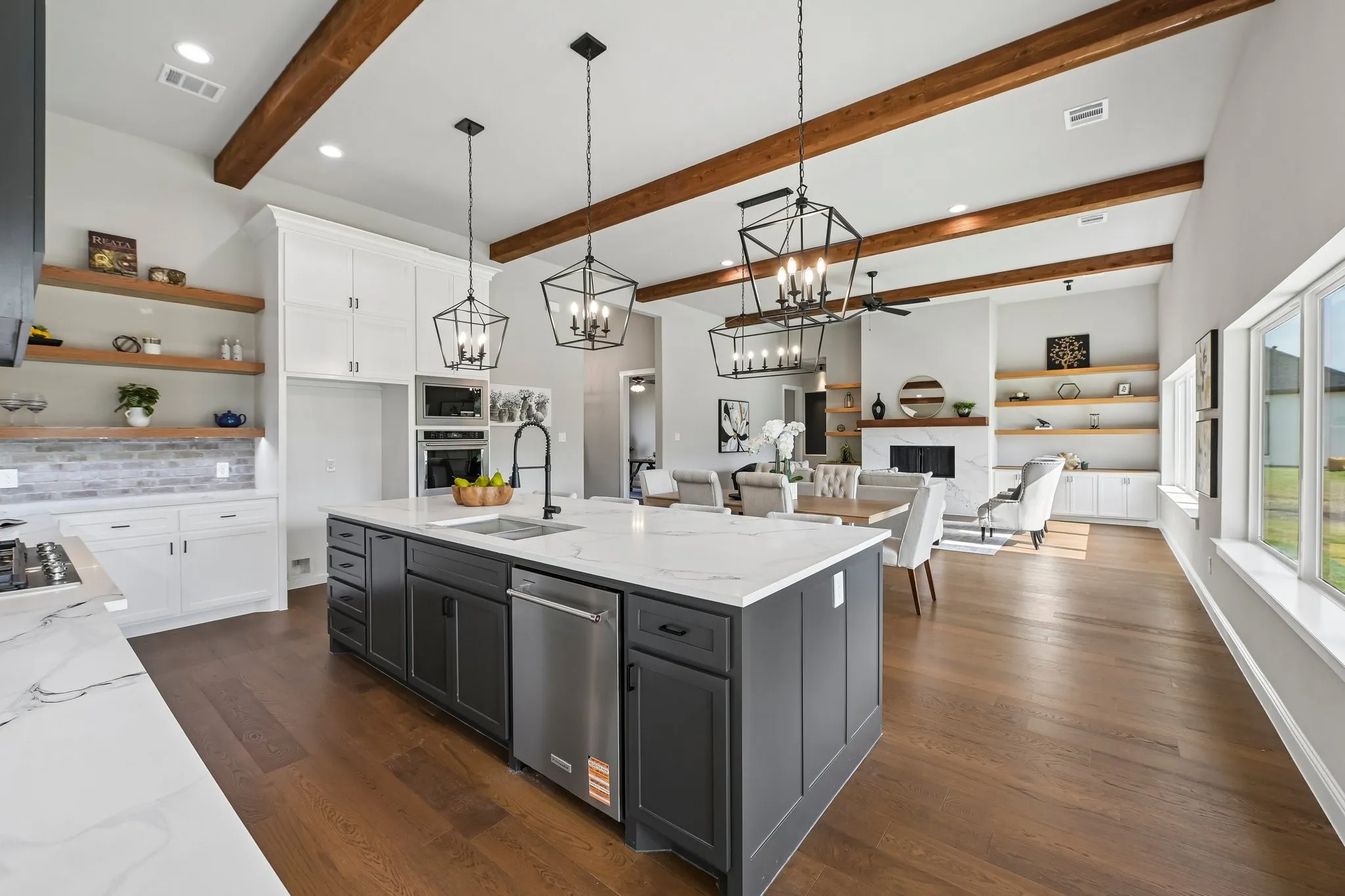 Vaulted ceiling with exposed wood beams, wood-finish flooring, white cabinetry, dark gray island with integrated sink, and white countertop