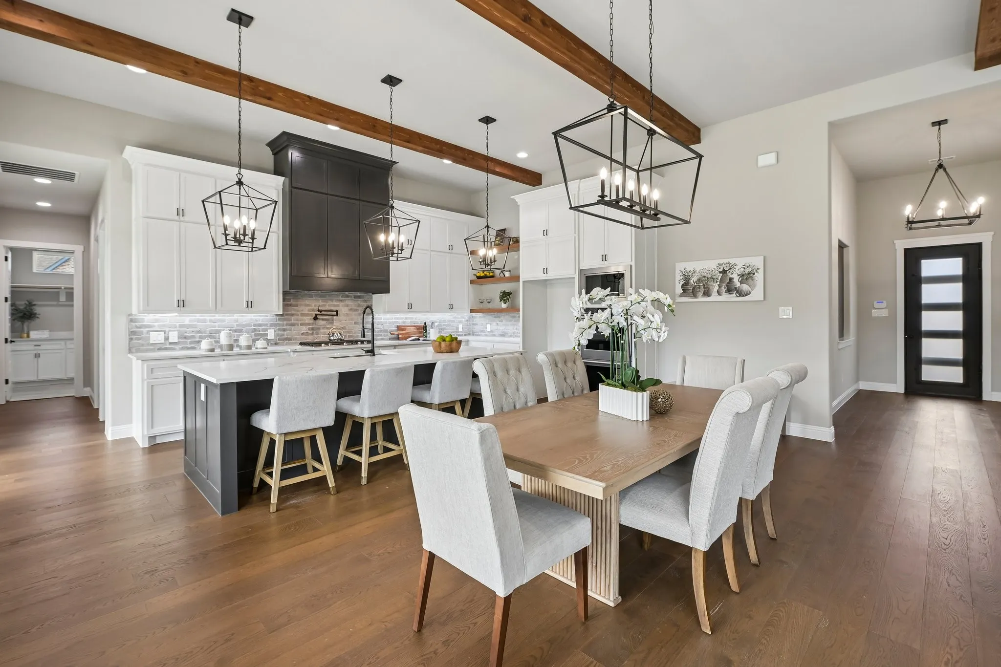 Spacious kitchen and dining area featuring wood-finish flooring, exposed ceiling beams, a kitchen island with seating, a dark range hood, and pendant lighting