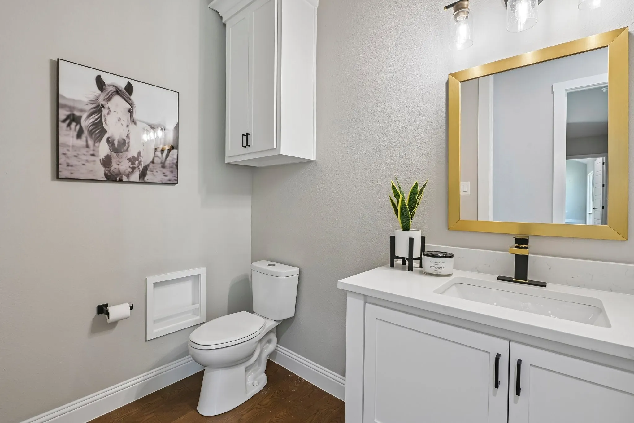 White vanity with under-mount sink, gold-framed mirror, and wood-finish flooring