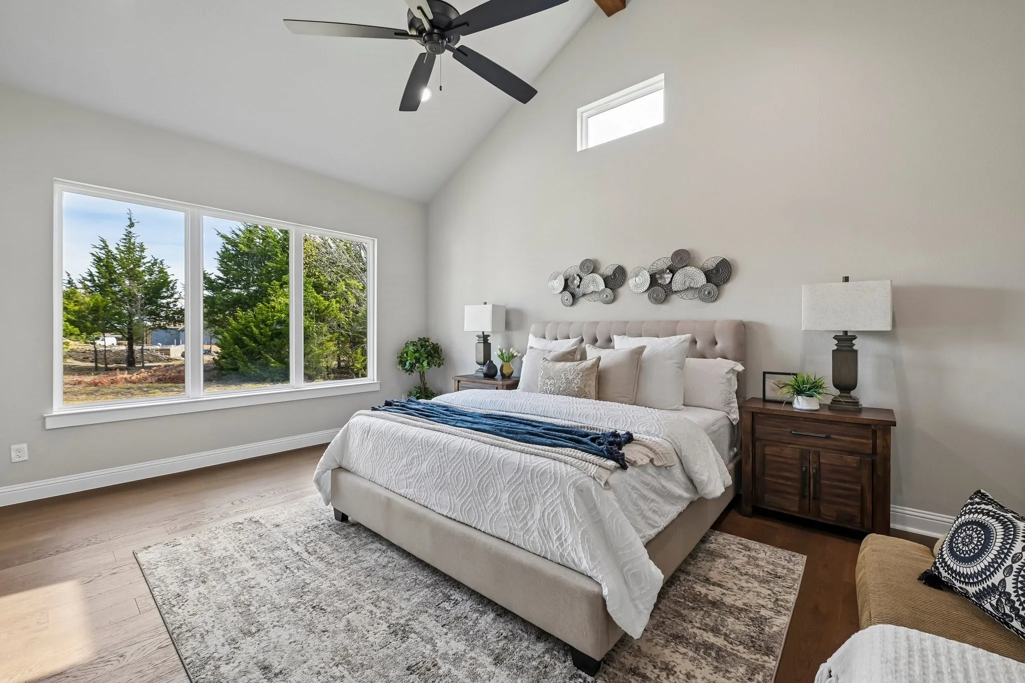 Vaulted ceiling with exposed wood beam, large picture windows, wood-finish flooring, and a ceiling fan