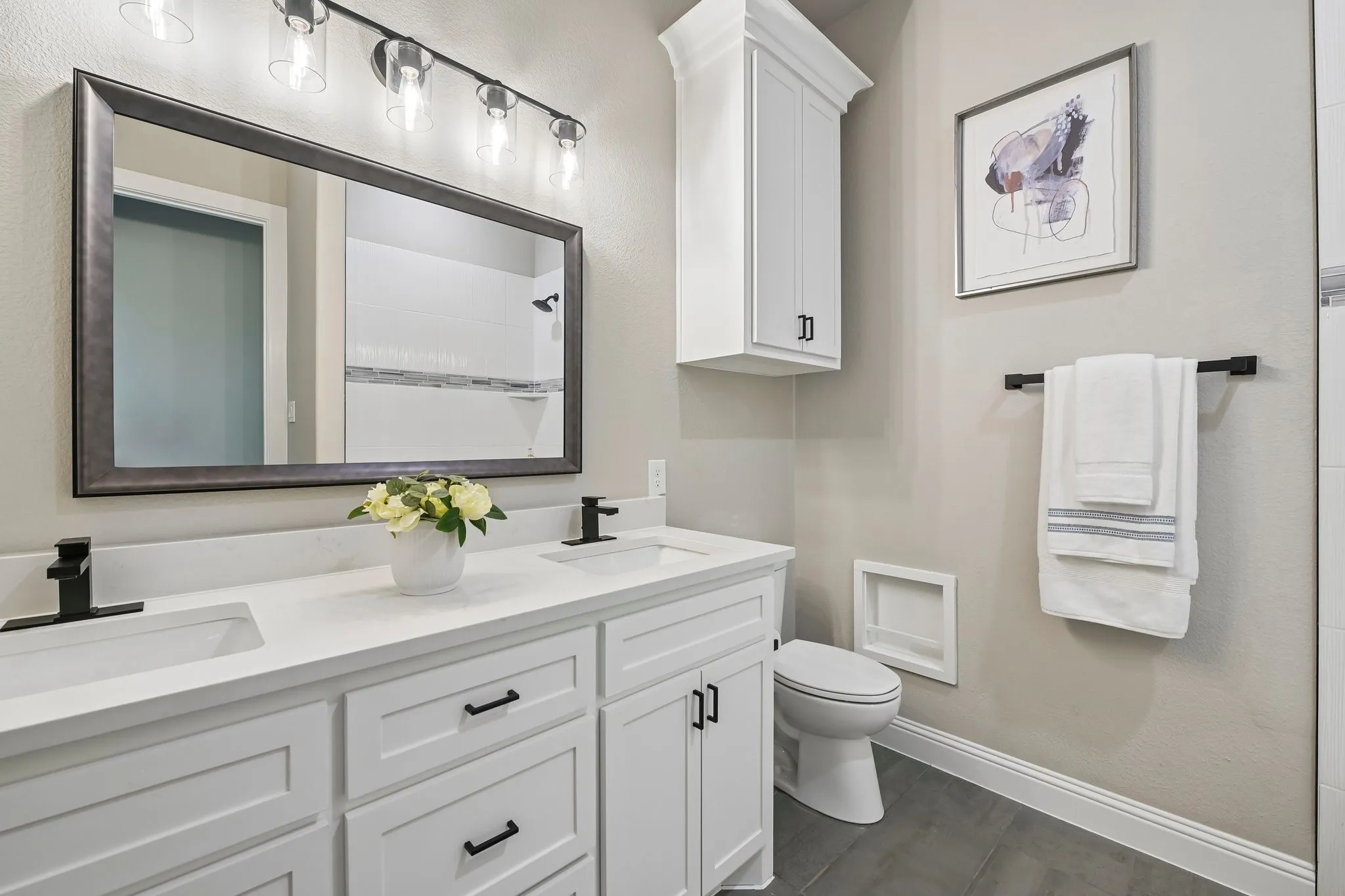 Double vanity with white cabinetry, matte black hardware, and an expansive framed mirror