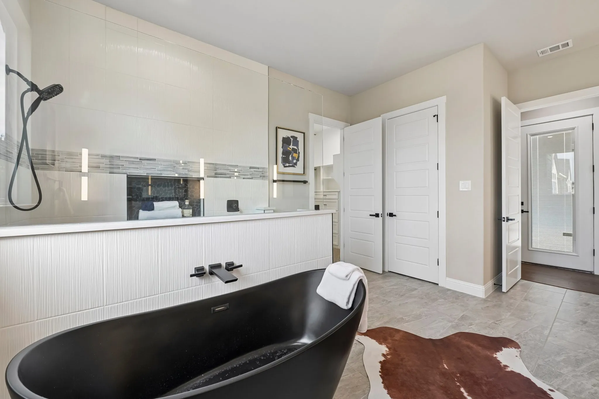 Freestanding black soaking tub, large format tile flooring, glass-enclosed shower with matte black fixtures, and white paneled doors