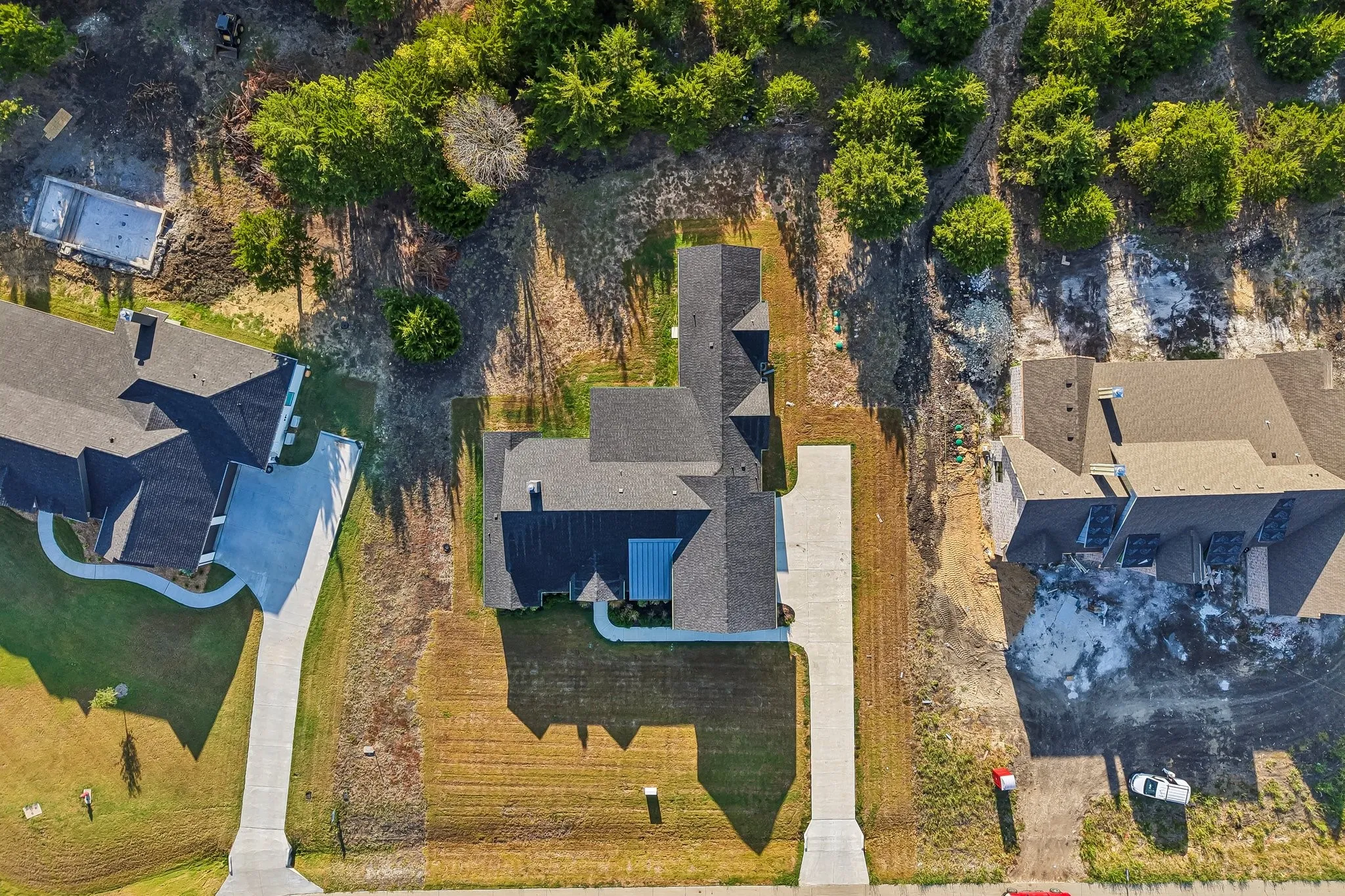 Property featuring a dark shingle roof, concrete driveway, and established trees in the surrounding landscape