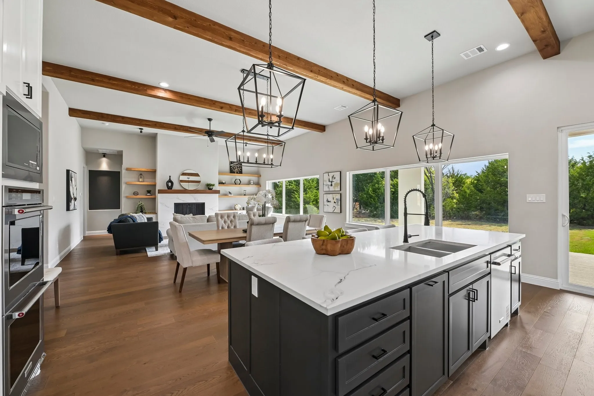 Vaulted ceilings with exposed wood beams, wood-finish flooring, and a kitchen island with a double basin sink and a matte black faucet