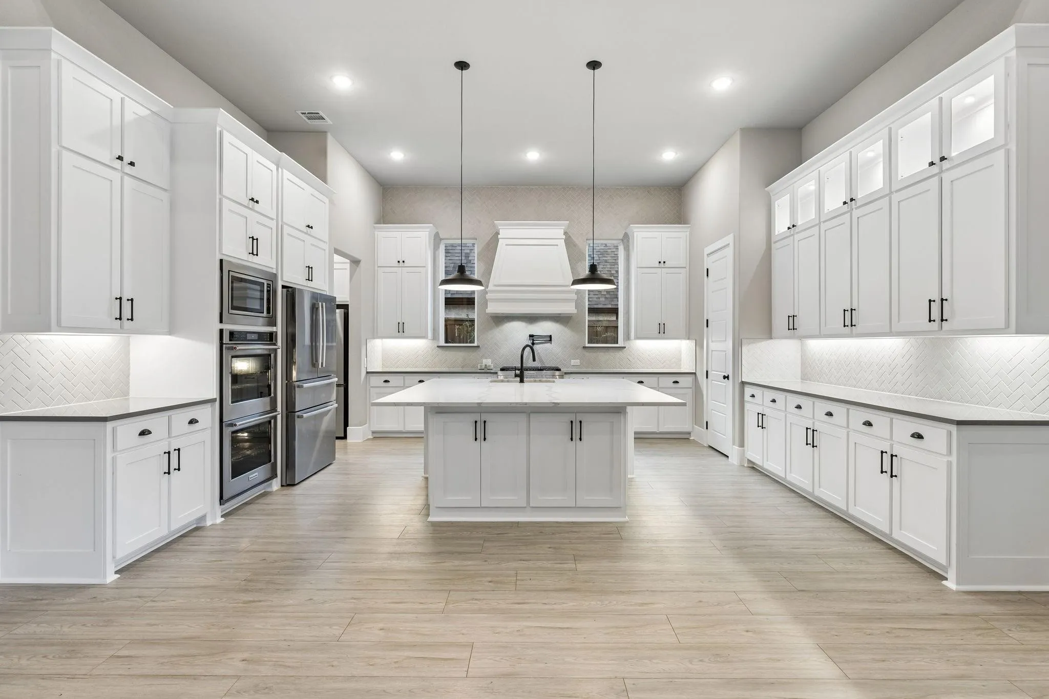 Spacious kitchen featuring white shaker cabinetry with matte black hardware, stainless steel appliances, a center island, and wood-finish flooring