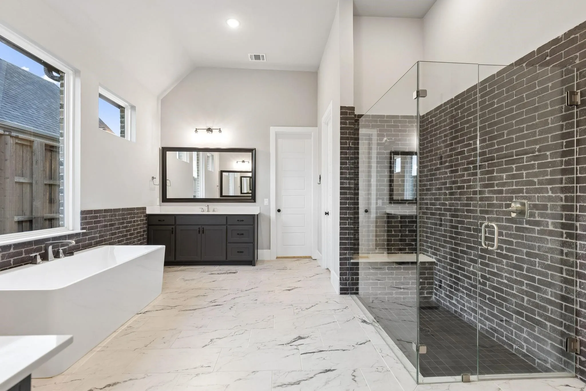 Spacious bathroom featuring a freestanding soaking tub, a large walk-in shower with a glass enclosure, a vanity with dual sinks, and patterned tile flooring