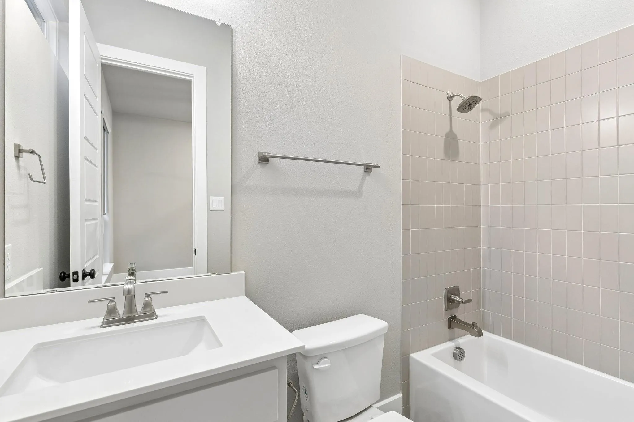 Vanity with integrated sink, brushed nickel faucet, frameless mirror, white subway tile shower surround, and a white soaking tub