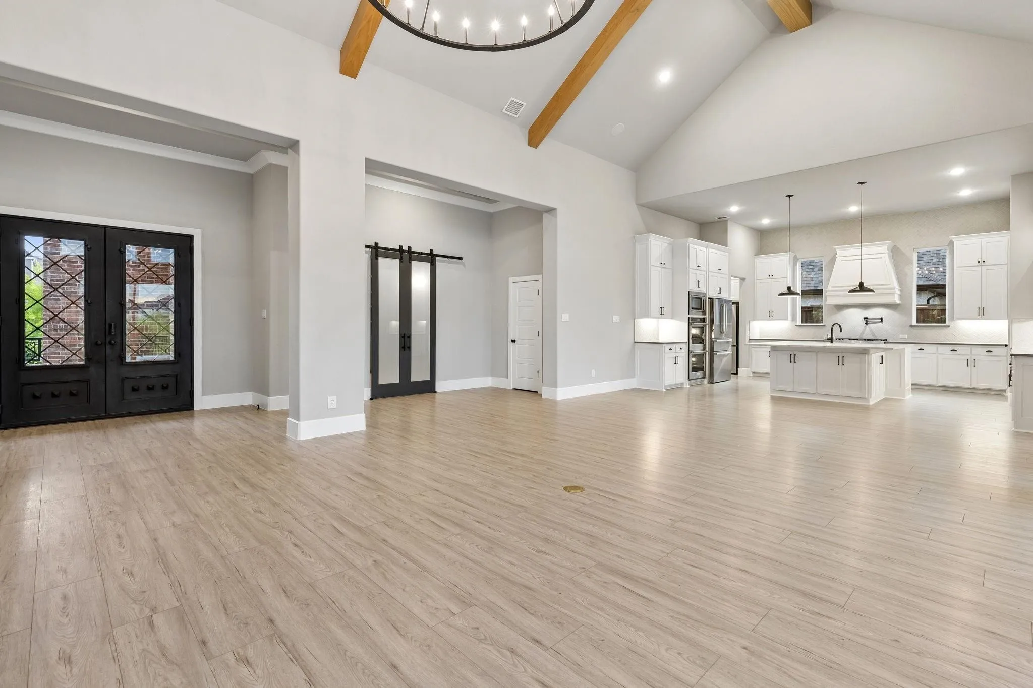 Vaulted ceilings with exposed wood beams, light wood-finish flooring, and double entry doors with decorative glass inserts
