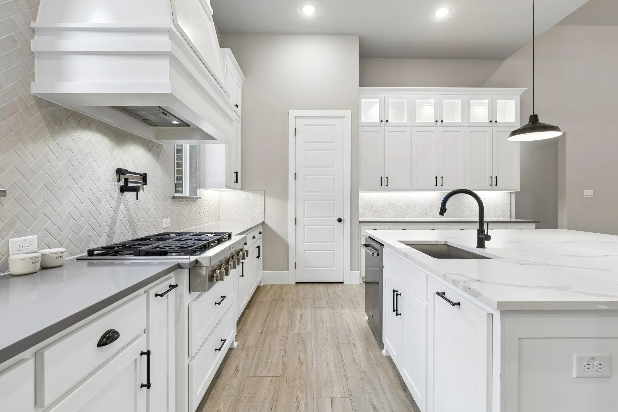 Kitchen featuring white cabinetry, light-colored wood-finish flooring, a herringbone pattern tile backsplash, a center island with sink, and a range with a pot filler