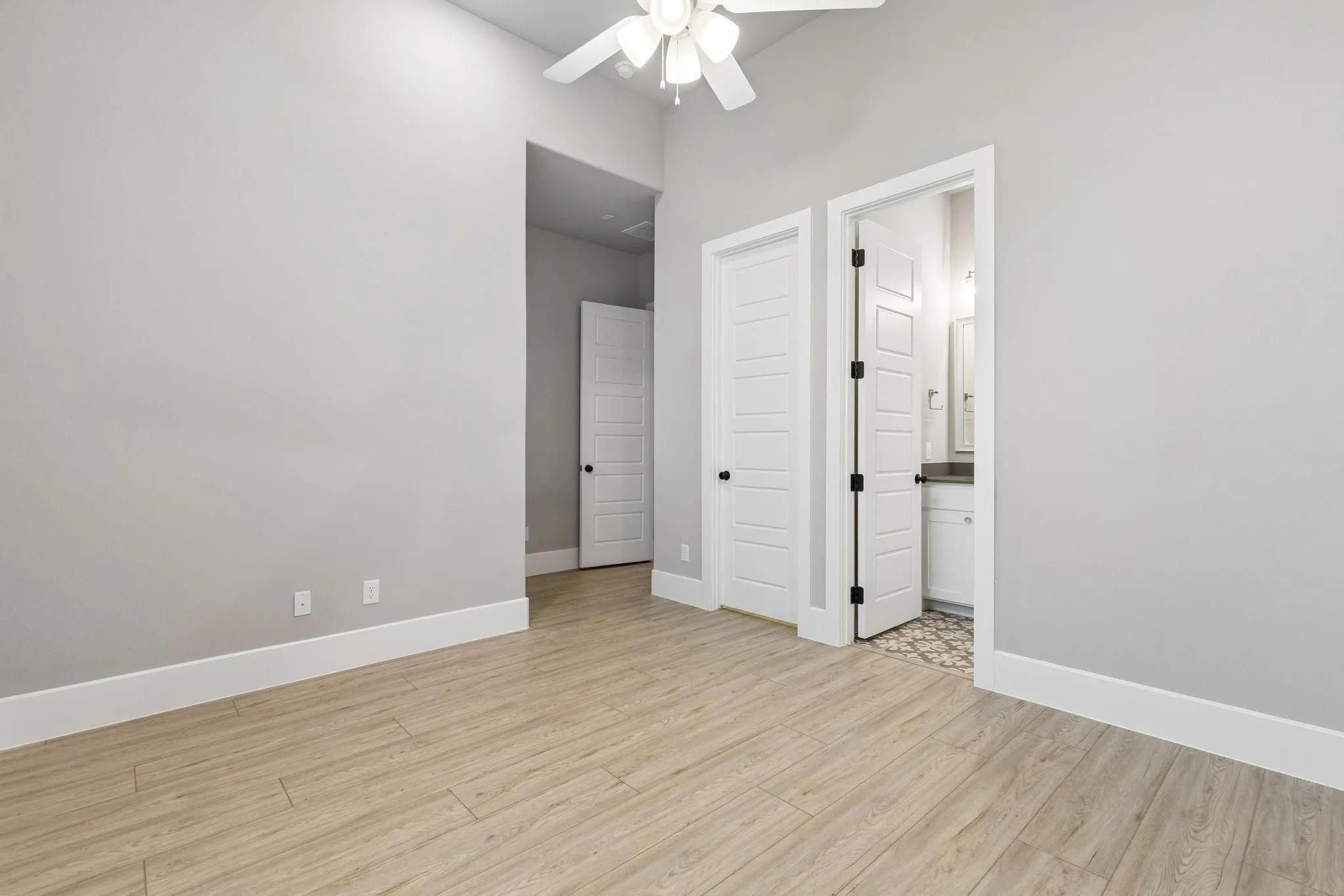 Wood-finish flooring, white trim, recessed entry, white paneled doors with black hardware, and an overhead ceiling fan