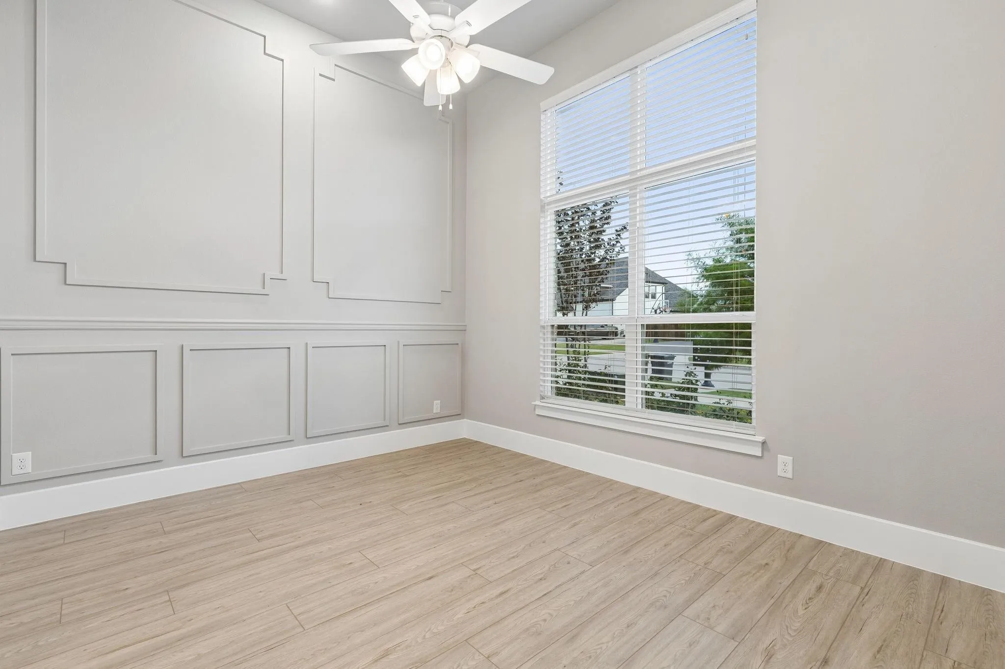 Tall window with blinds, wood-finish flooring, decorative wall molding, and a ceiling fan