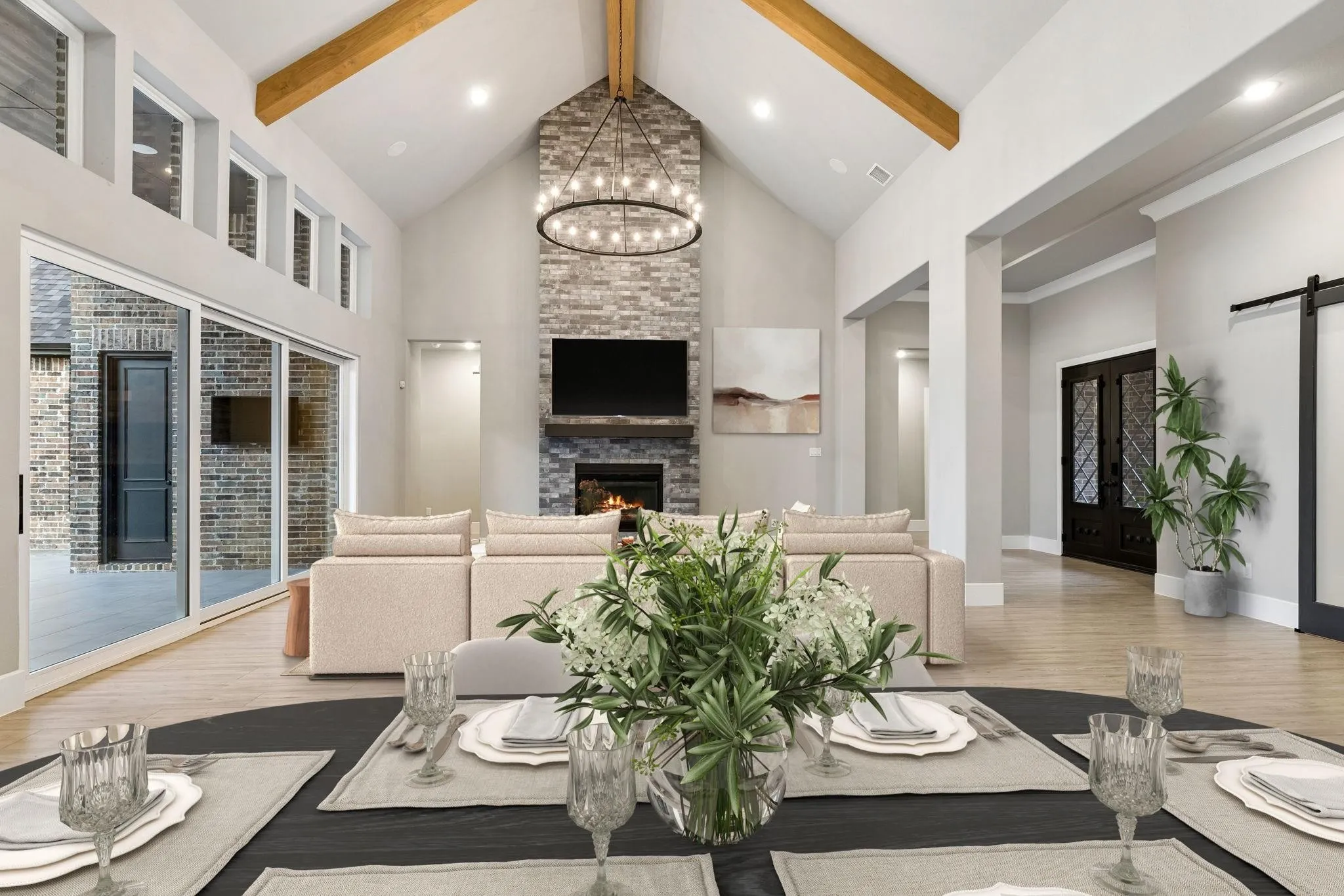 Vaulted ceiling with exposed wood beams, stone fireplace, oversized sliding glass doors, transom windows, and wood-finish flooring